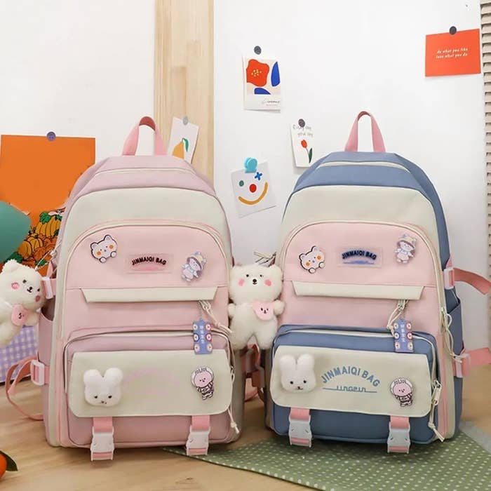 Dos mochilas con peluches pequeños: una rosa con conejo y carita de gato, otra azul con conejo y etiqueta "JINHAOJI BAG". Decoración adorable
