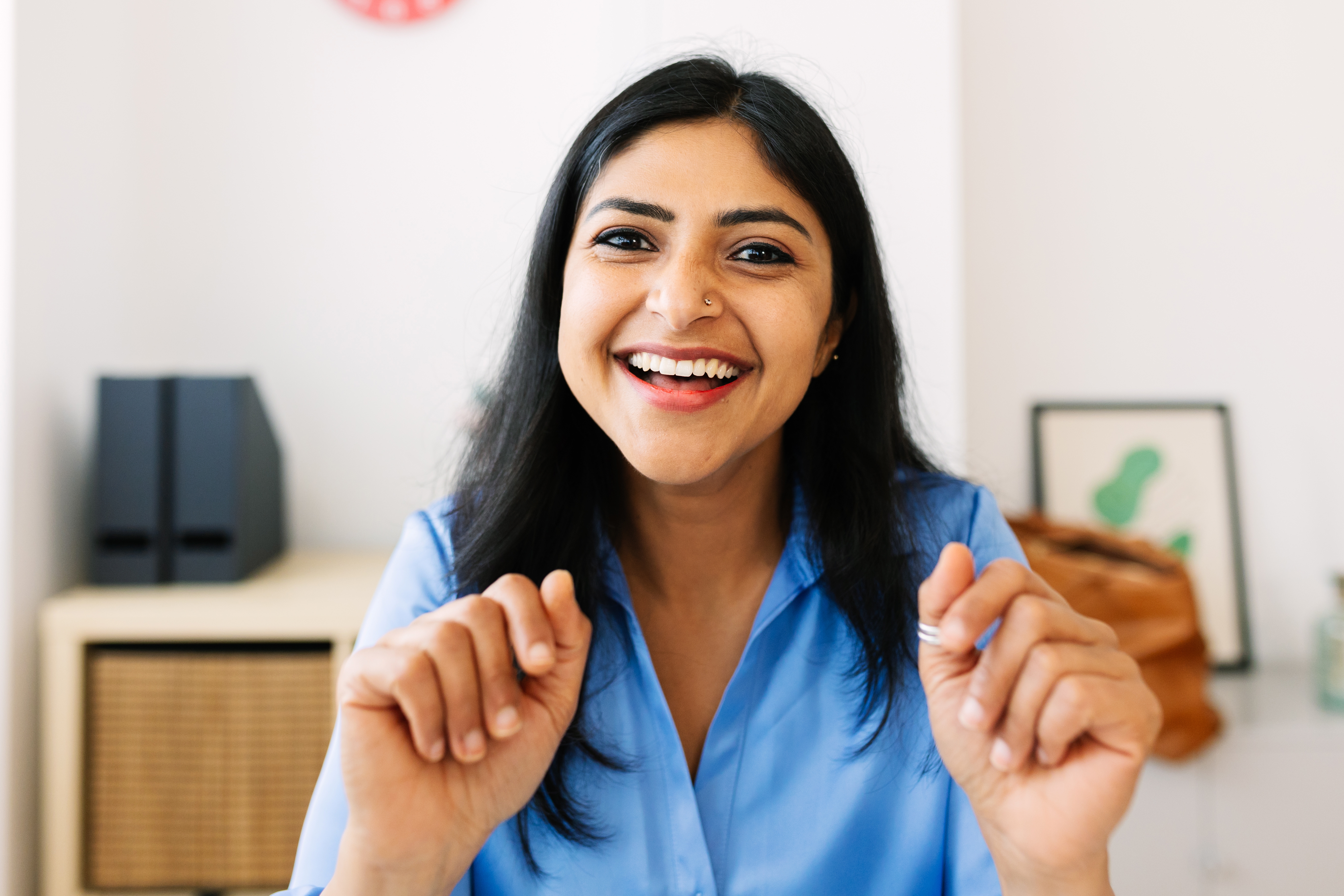 Personen smiler bredt mens han sitter ved et skrivebord, har på seg en knapp-up-skjorte, utstråler en gledelig og innbydende stemning