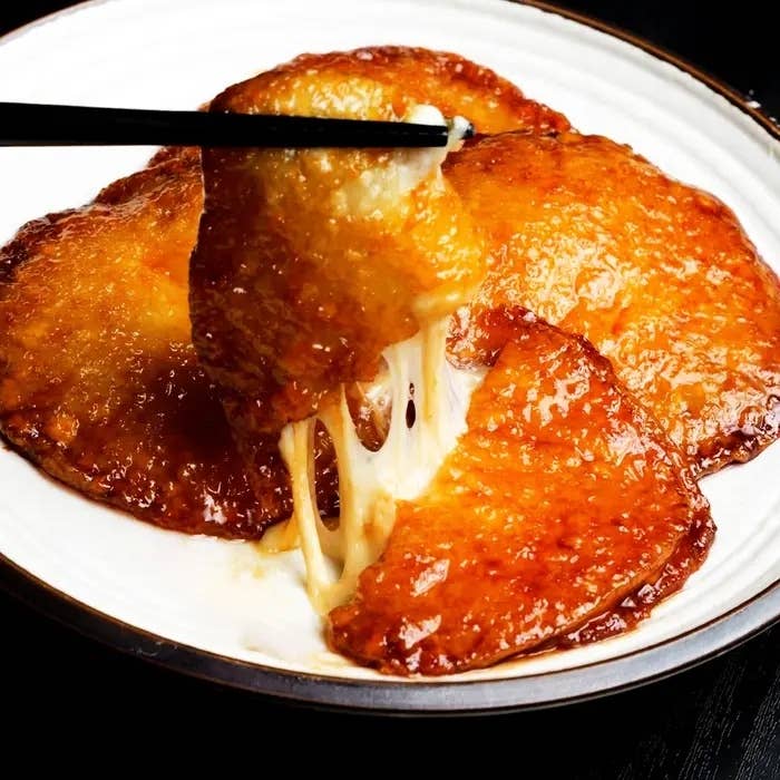 箸で引き伸ばされたチーズが乗った焼いたお餅が皿に盛られている。