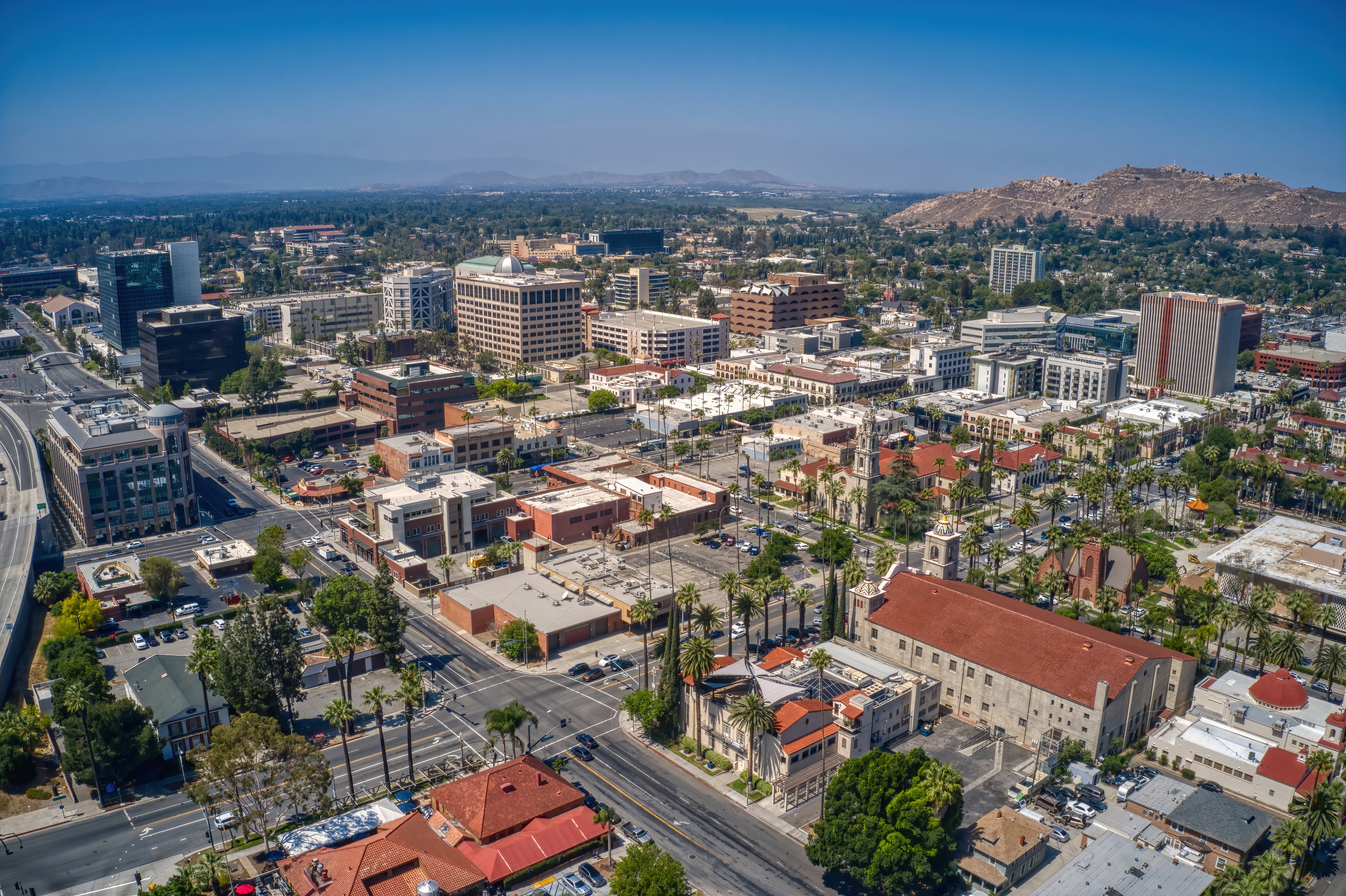 Aerial view of a cityscape featuring urban buildings, roads, and hills in the distance under a clear sky