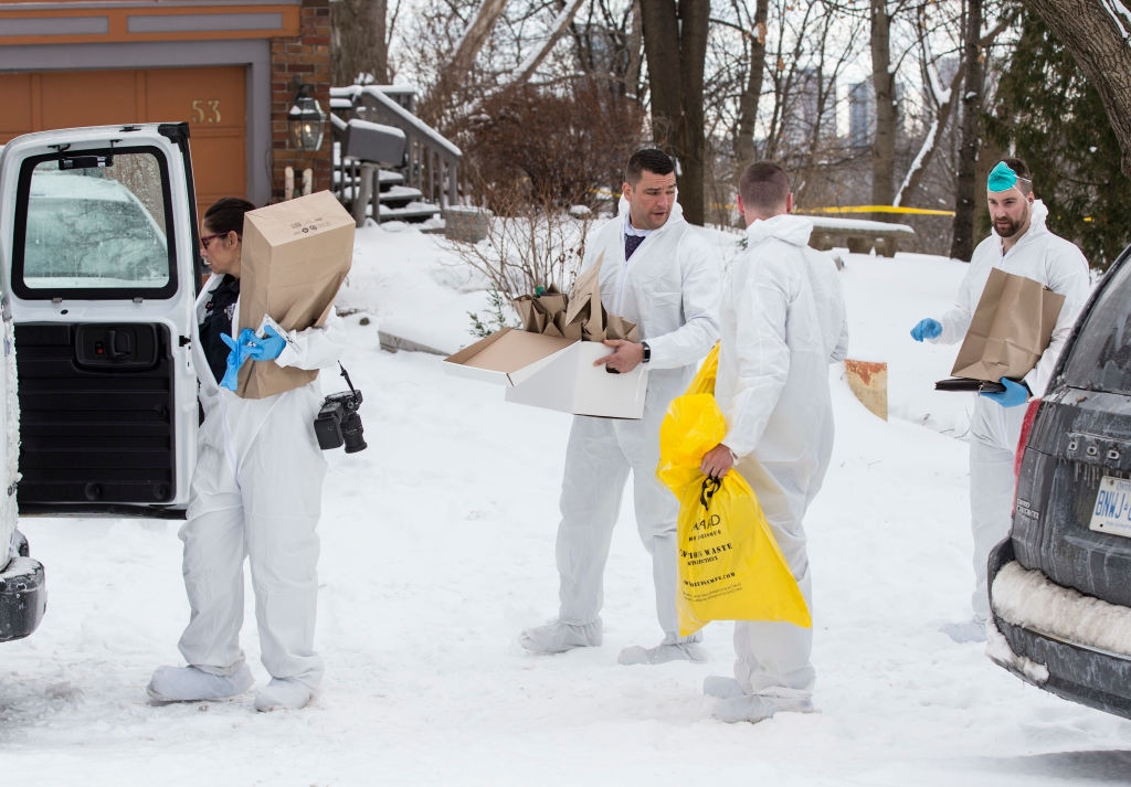 People in white protective suits gather items in a snowy residential area, placing them into a van