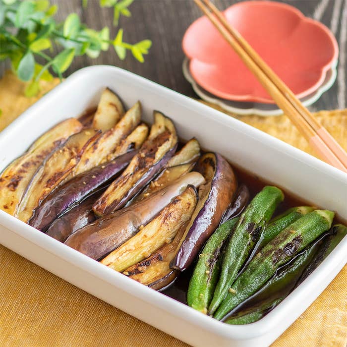 焼きナスとオクラの煮物が白い器に盛られている。背景に箸と花が添えられている。