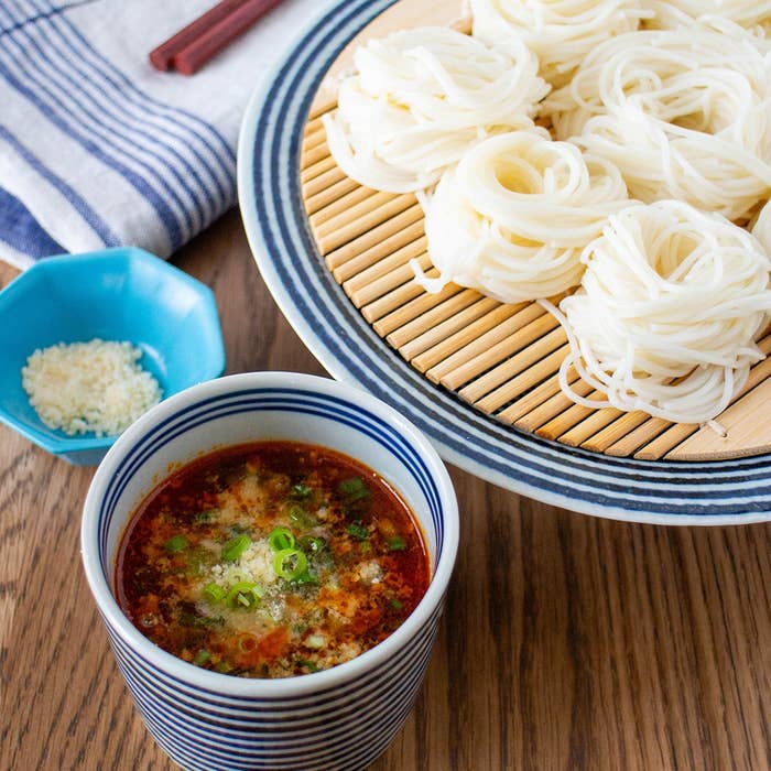 ざるに盛られた冷やしそうめんとたれ。薬味が添えられ、一緒に食べる準備が整っている。