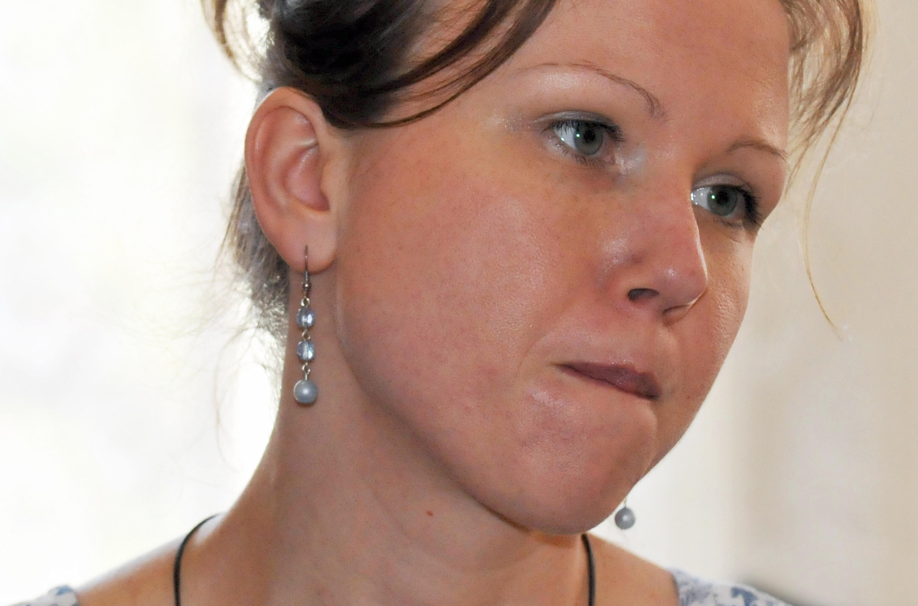 Person biting their lip with a thoughtful expression, wearing dangling earrings and a necklace