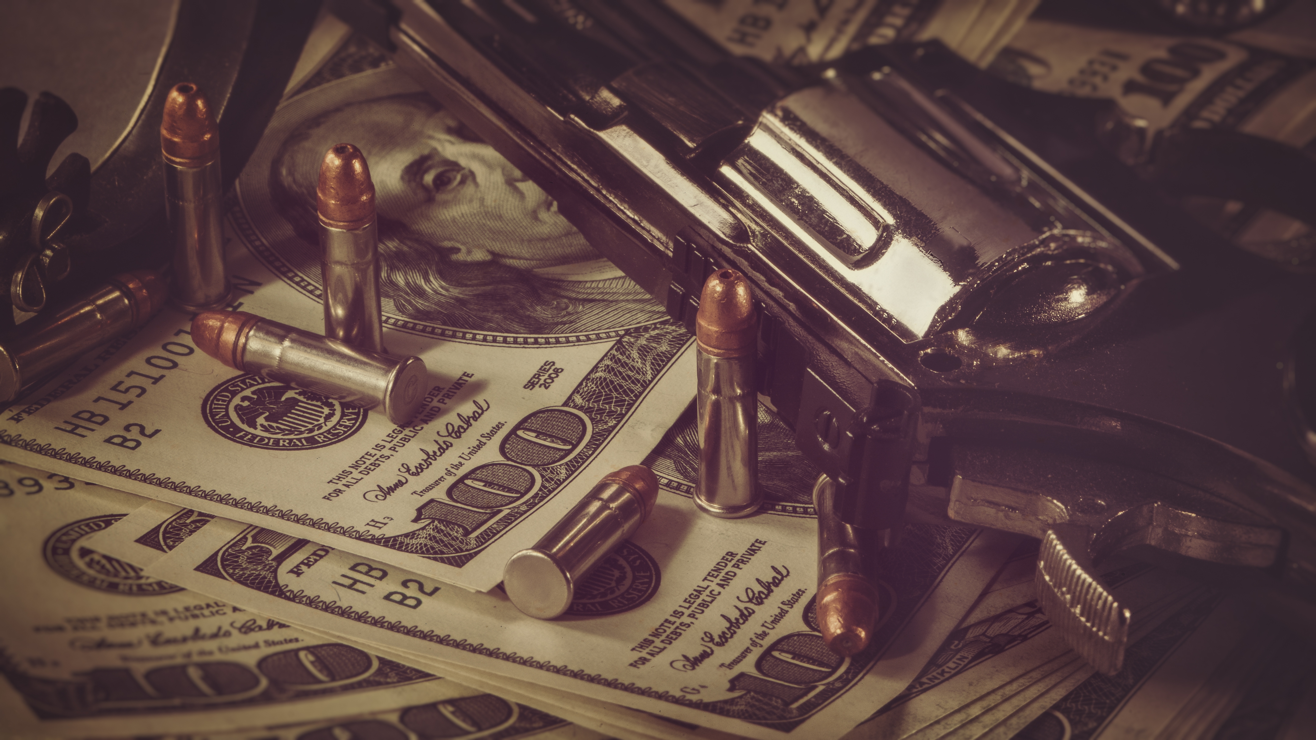 A handgun and bullets sit on a pile of hundred-dollar bills, suggesting themes of crime or wealth