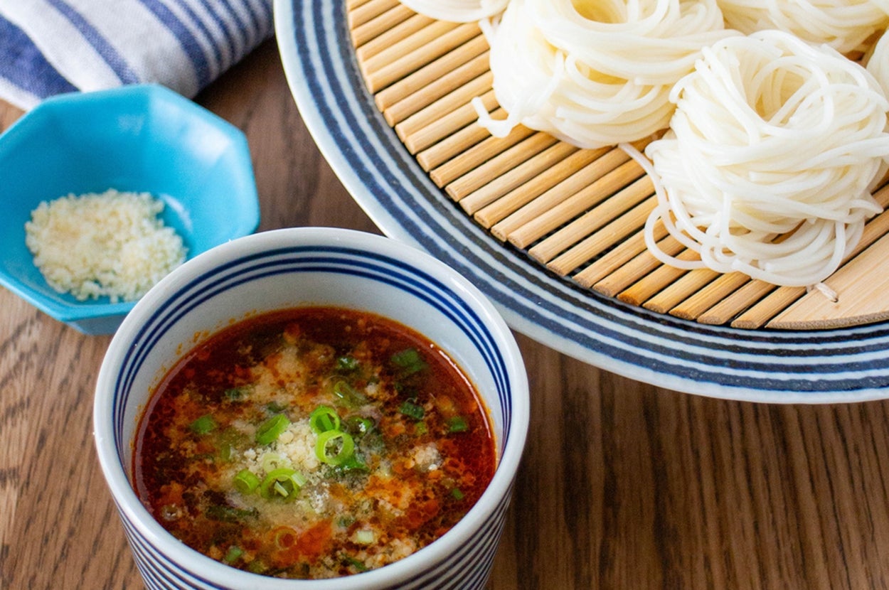 冷製そうめんと薬味入りのつけ汁がテーブルに置かれている。青の小皿には薬味が入っている。