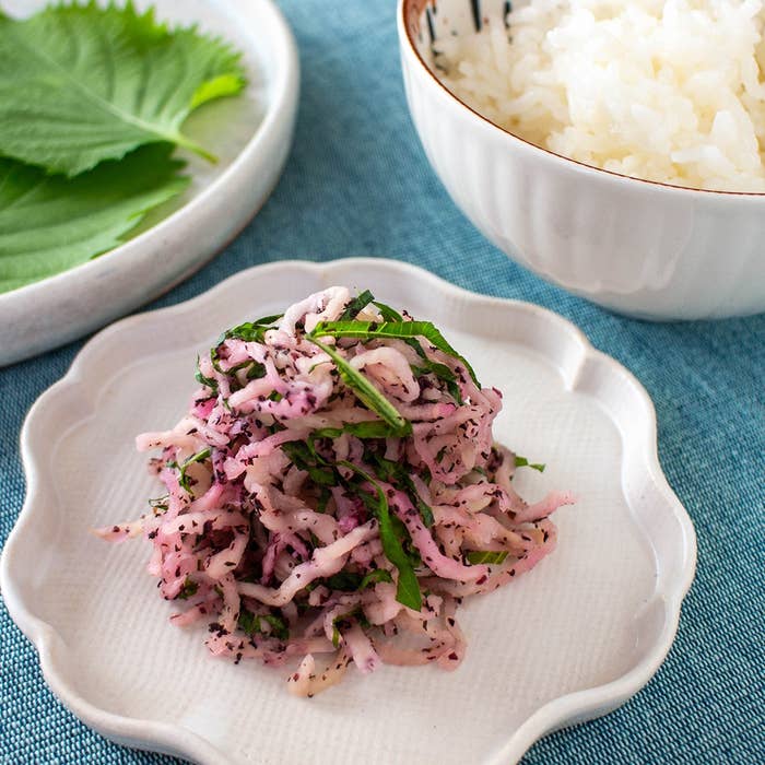 大根としそ葉の和え物が皿に盛られ、近くに白ご飯としそ葉が置かれている。
