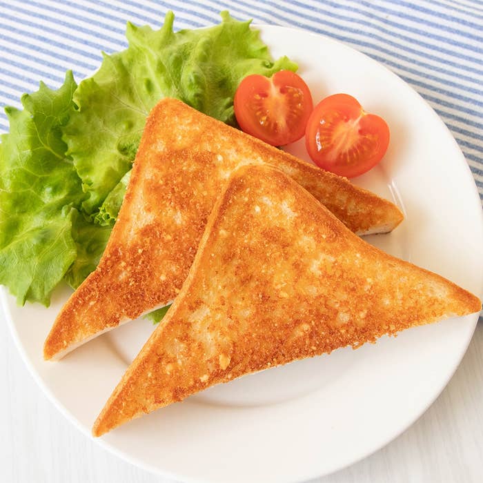 皿に盛られた焼きたての粉チーズバタートーストと、レタス、半分に切ったトマト。