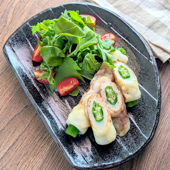 料理の盛り付け。チーズとオクラとちくわとミニトマト入りのサラダが黒い皿にのせられている。