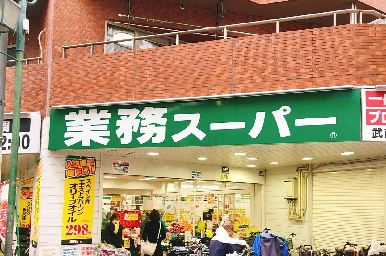 業務スーパーの外観。価格付き広告と買い物客が見られる。