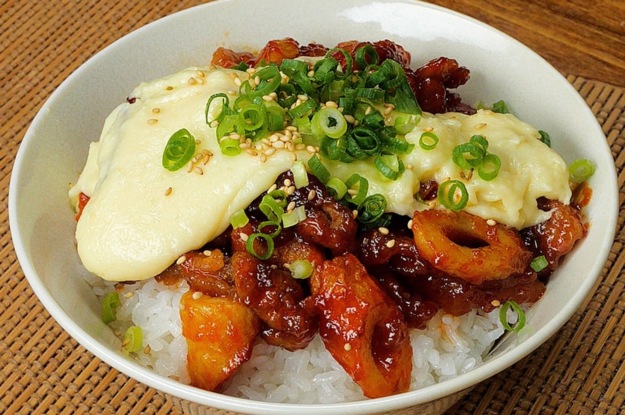 ご飯の上に、チキンとソースが載った丼。ネギが散らされている。
