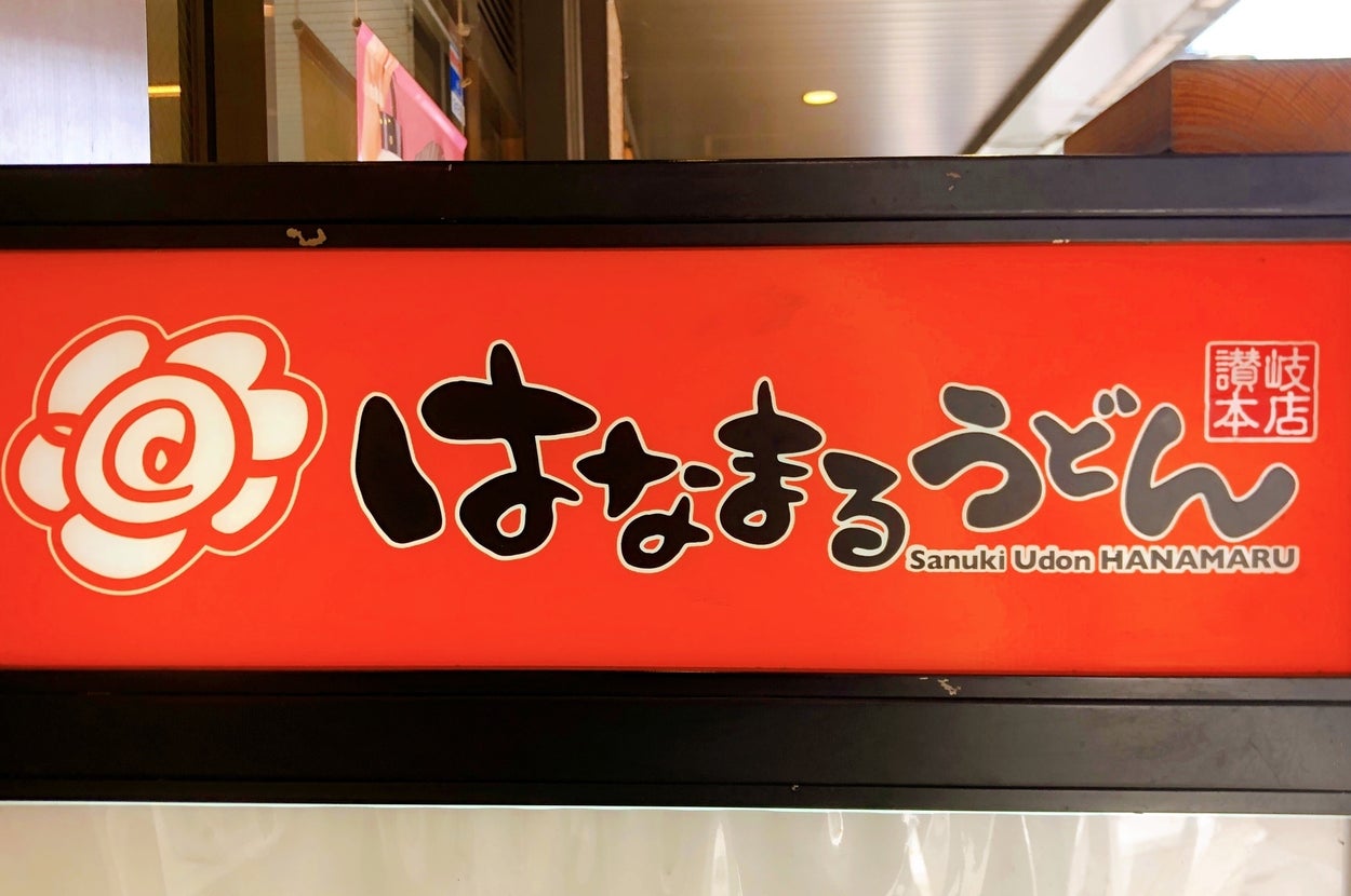 うどんチェーン店「はなまるうどん」看板。赤い背景に店名とロゴ、讃岐本店の文字。