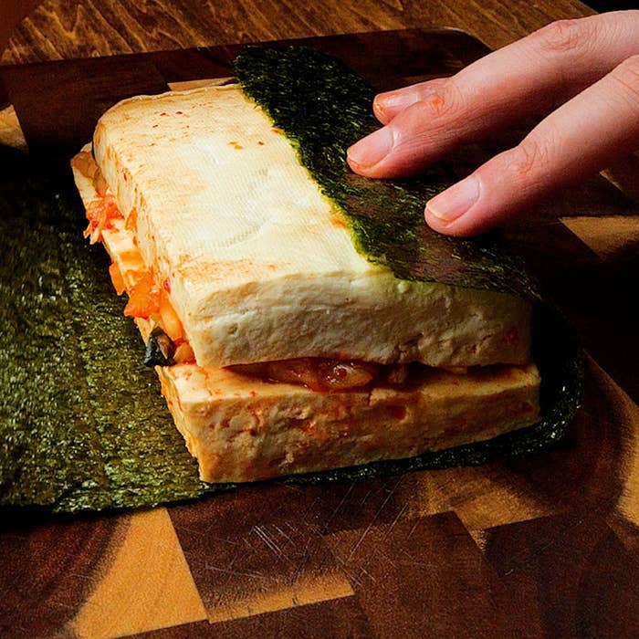 手でキムチと豆腐をのせた海苔を巻く準備をしている。