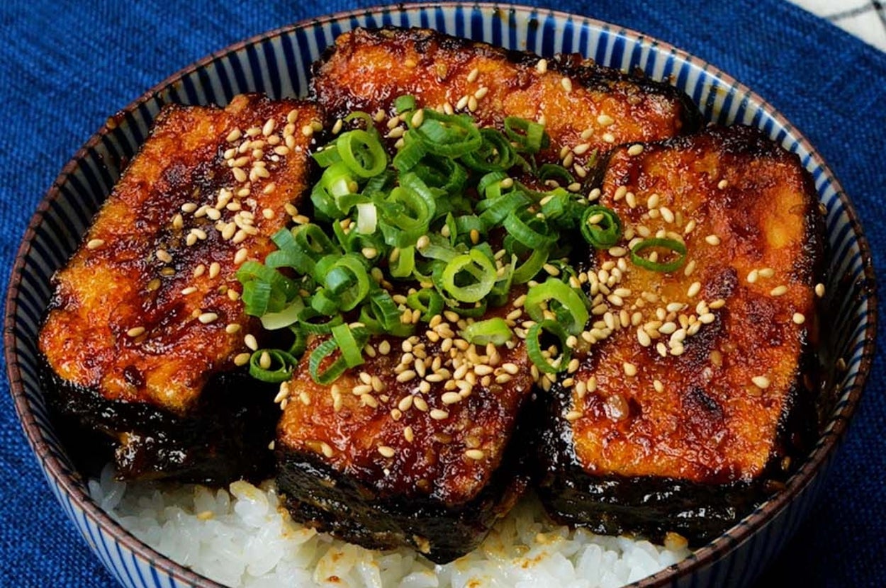 うなぎの蒲焼きが盛られたご飯の上にネギとゴマがトッピングされている丼。