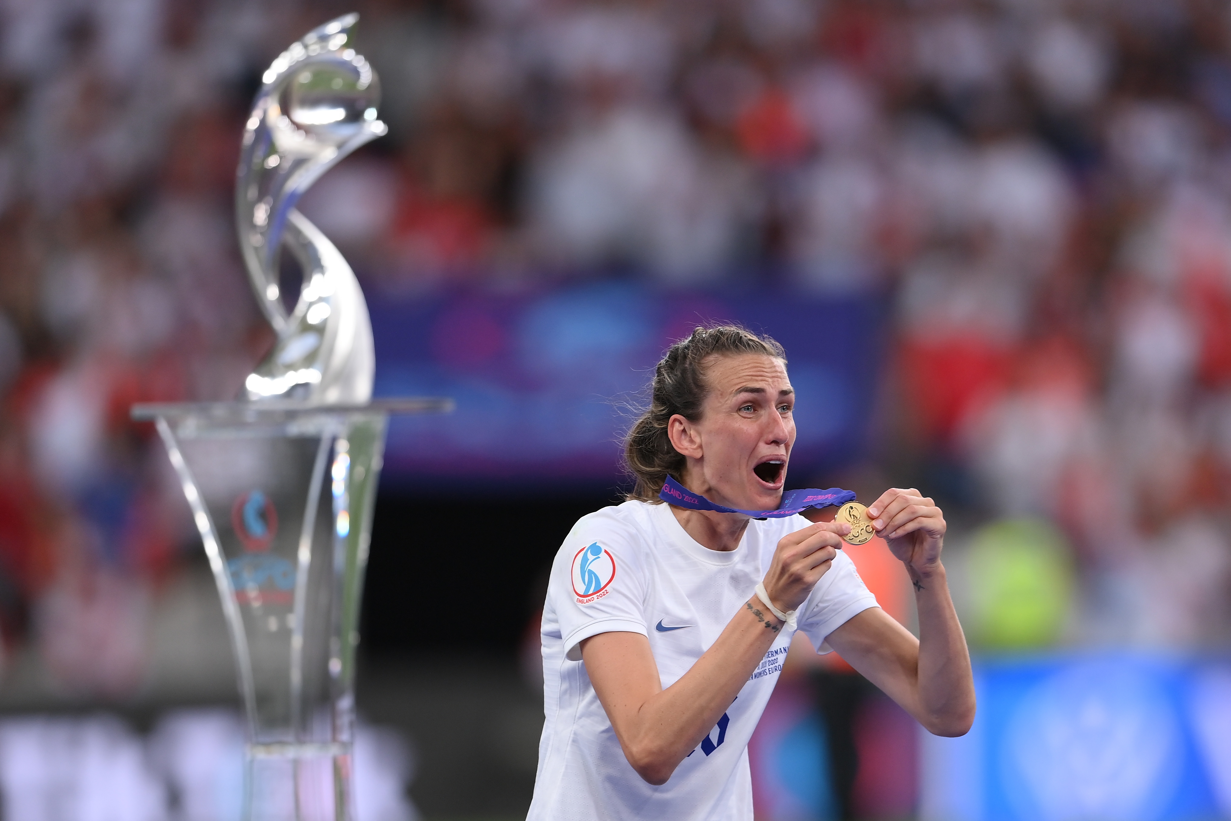 Athlete celebrates on field with a medal, wearing a jersey next to a tall, abstract trophy