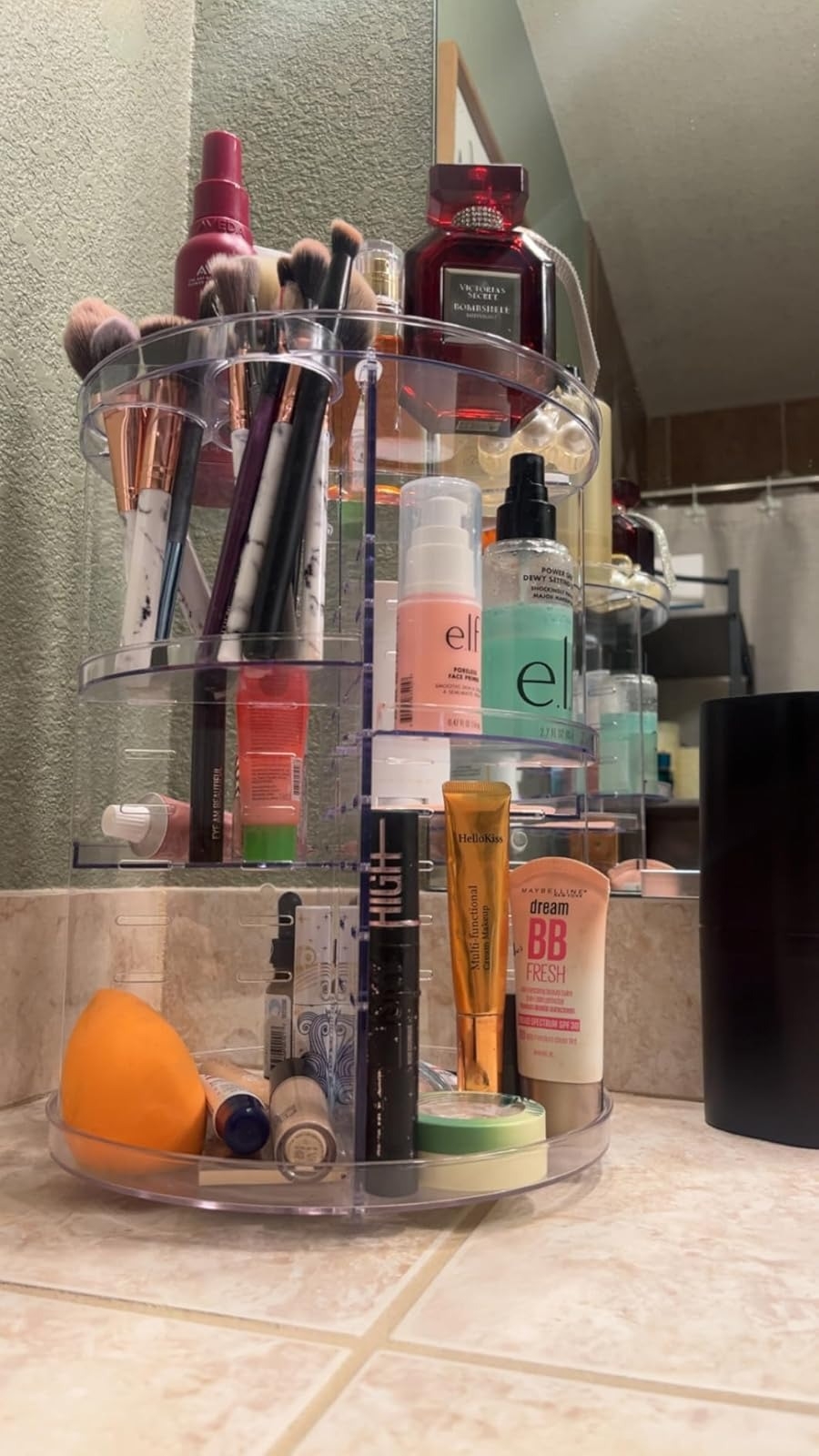 Vanity countertop with rotating organizer holding various makeup and skincare products, including brushes, creams, and serums