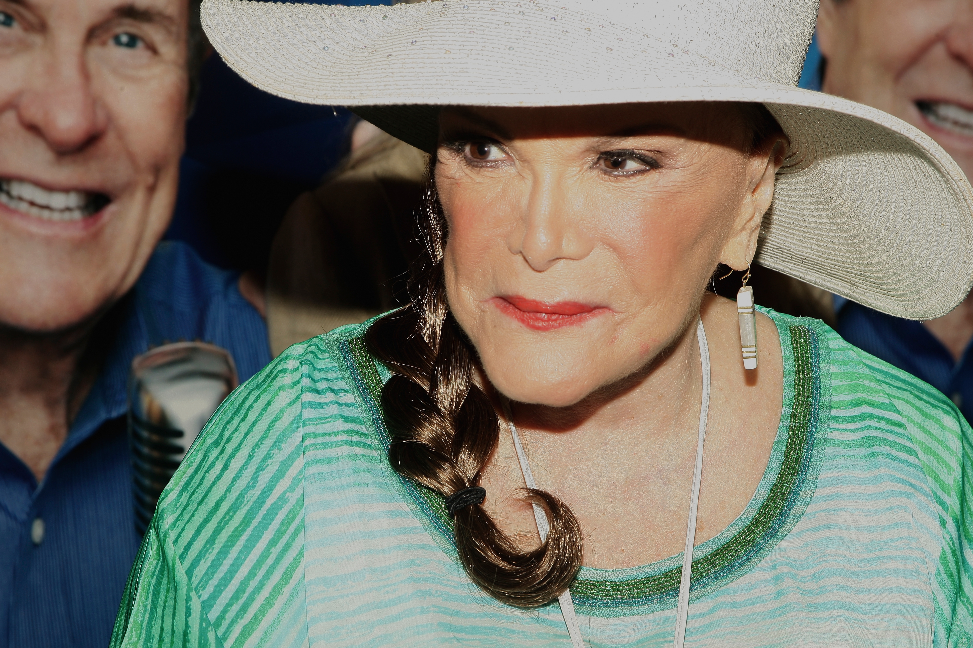 Connie Francis in a wide-brimmed hat and striped outfit, wearing earrings, with two smiling individuals in the background