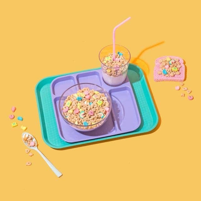 Un tazón y un vaso con cereales junto a una cuchara y una galleta decorada sobre bandejas de comida