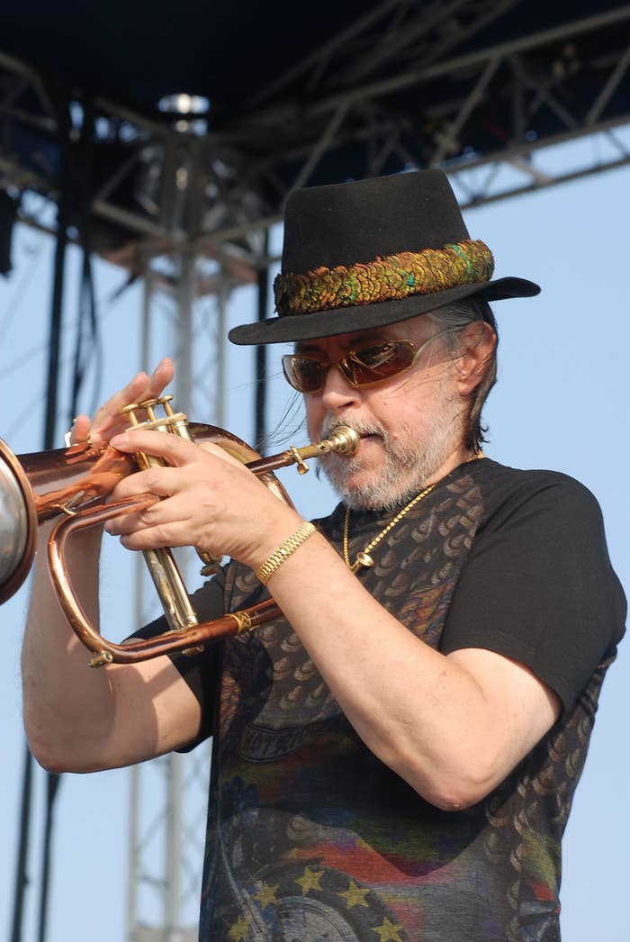 Chuck Mangione wearing a hat and sunglasses plays a trumpet on stage during a live performance