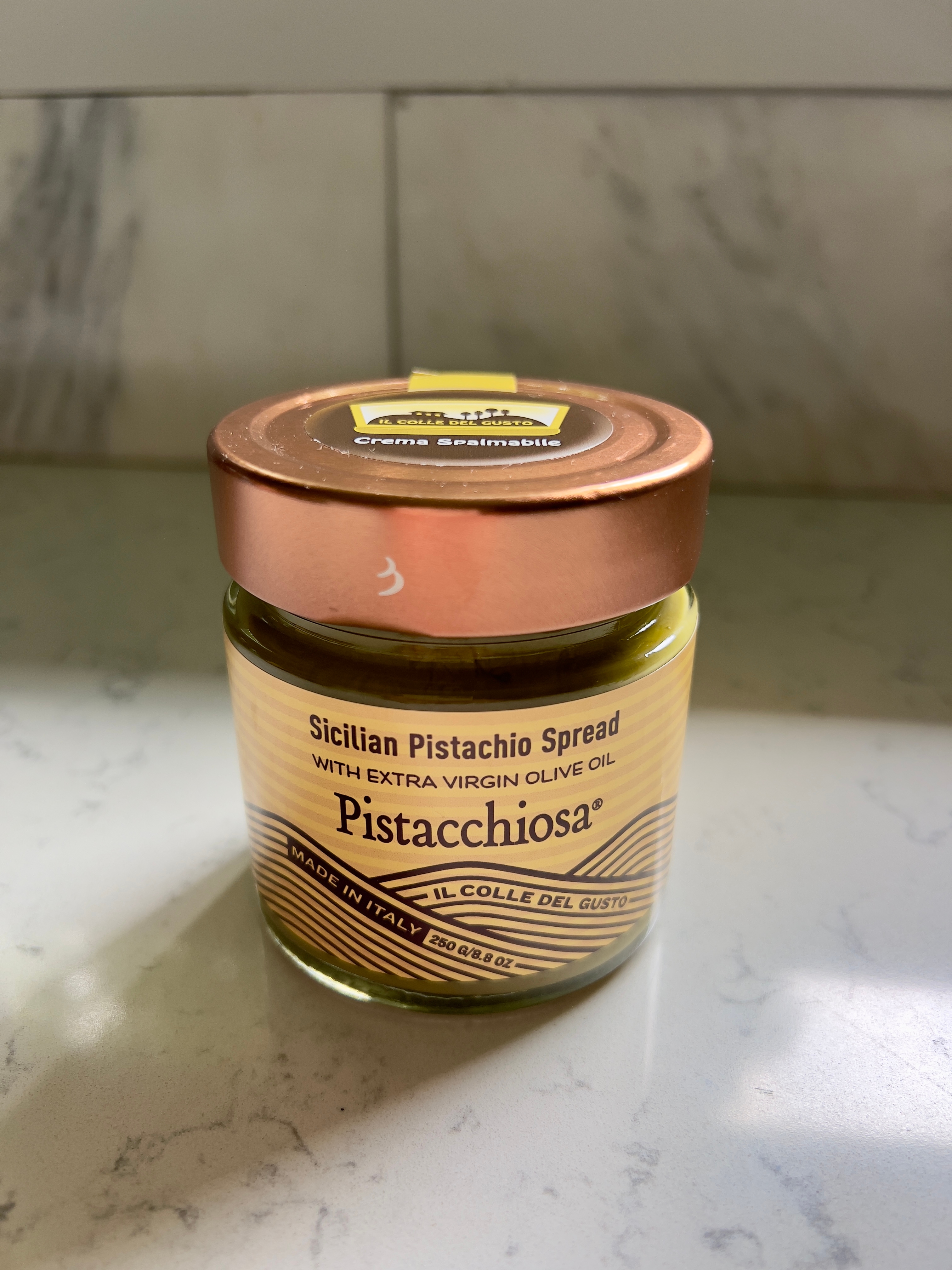 Jar of Sicilian pistachio spread labeled "Pistacchiosa" with extra virgin olive oil, made in Italy, on a countertop