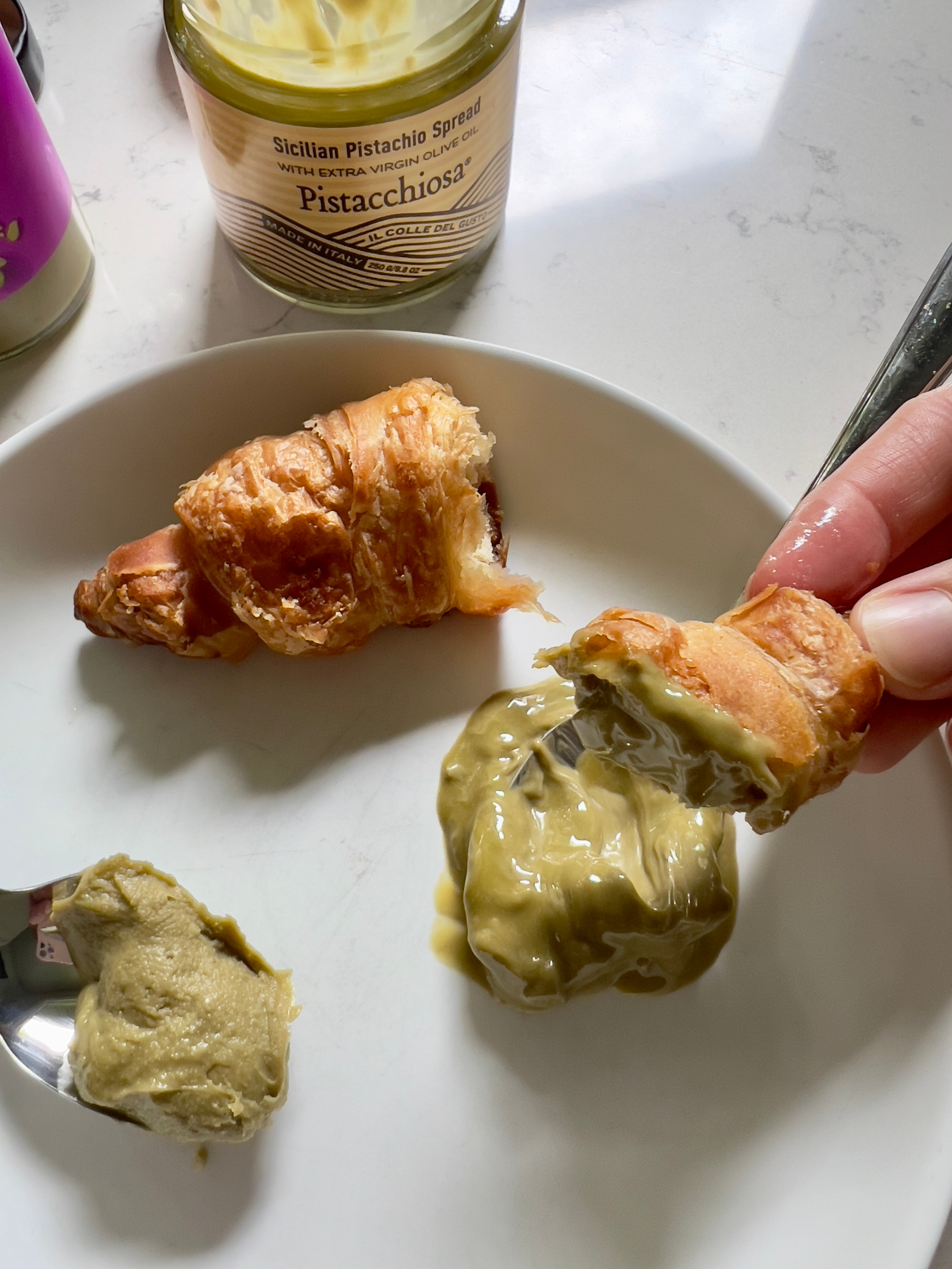 Croissant pieces on a plate with a Sicilian pistachio spread jar nearby, highlighting a gourmet breakfast or snack scene