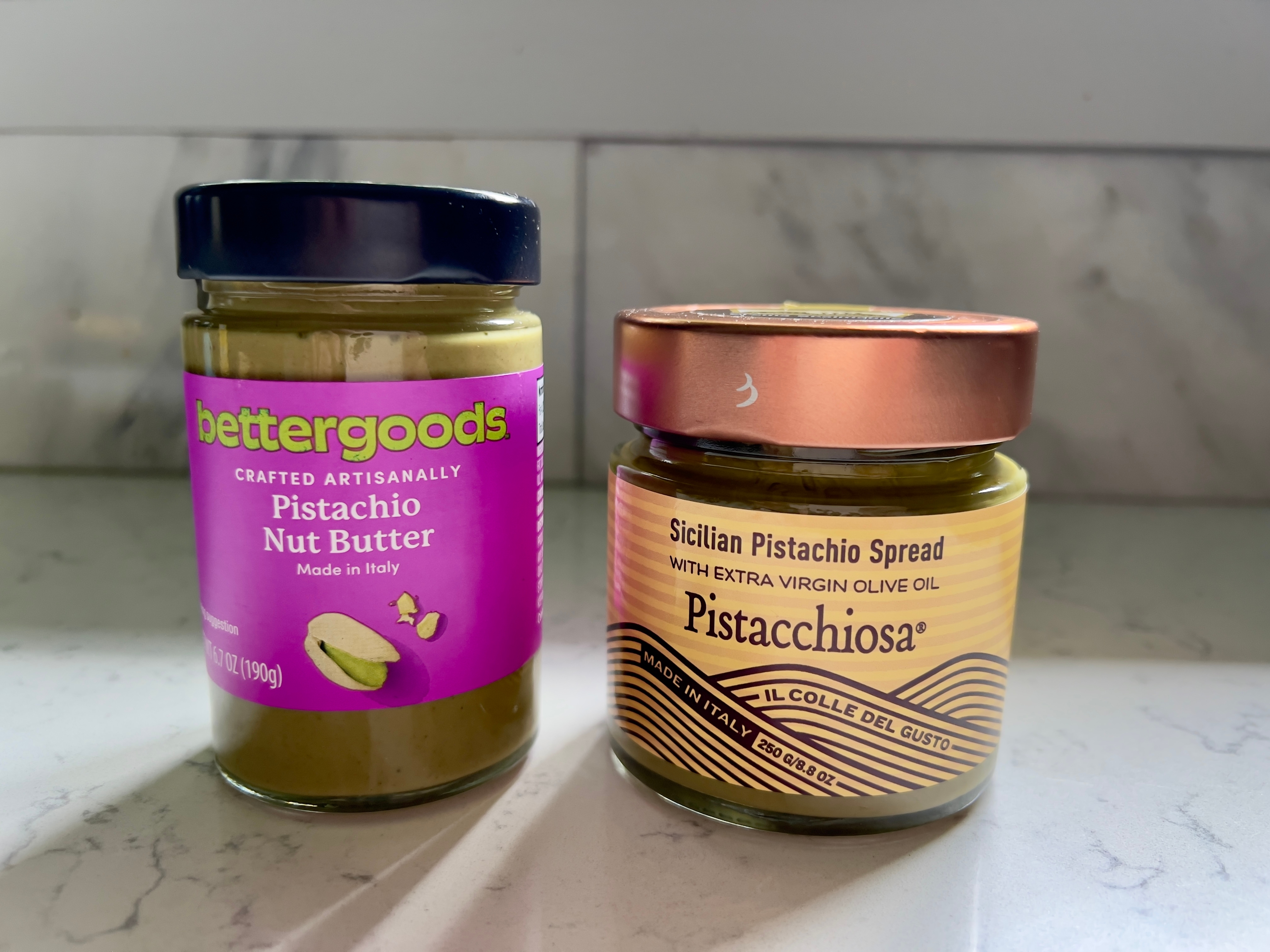 Two jars of pistachio spread on a counter: one labeled "Pistachio Nut Butter," the other "Sicilian Pistachio Spread with Extra Virgin Olive Oil."