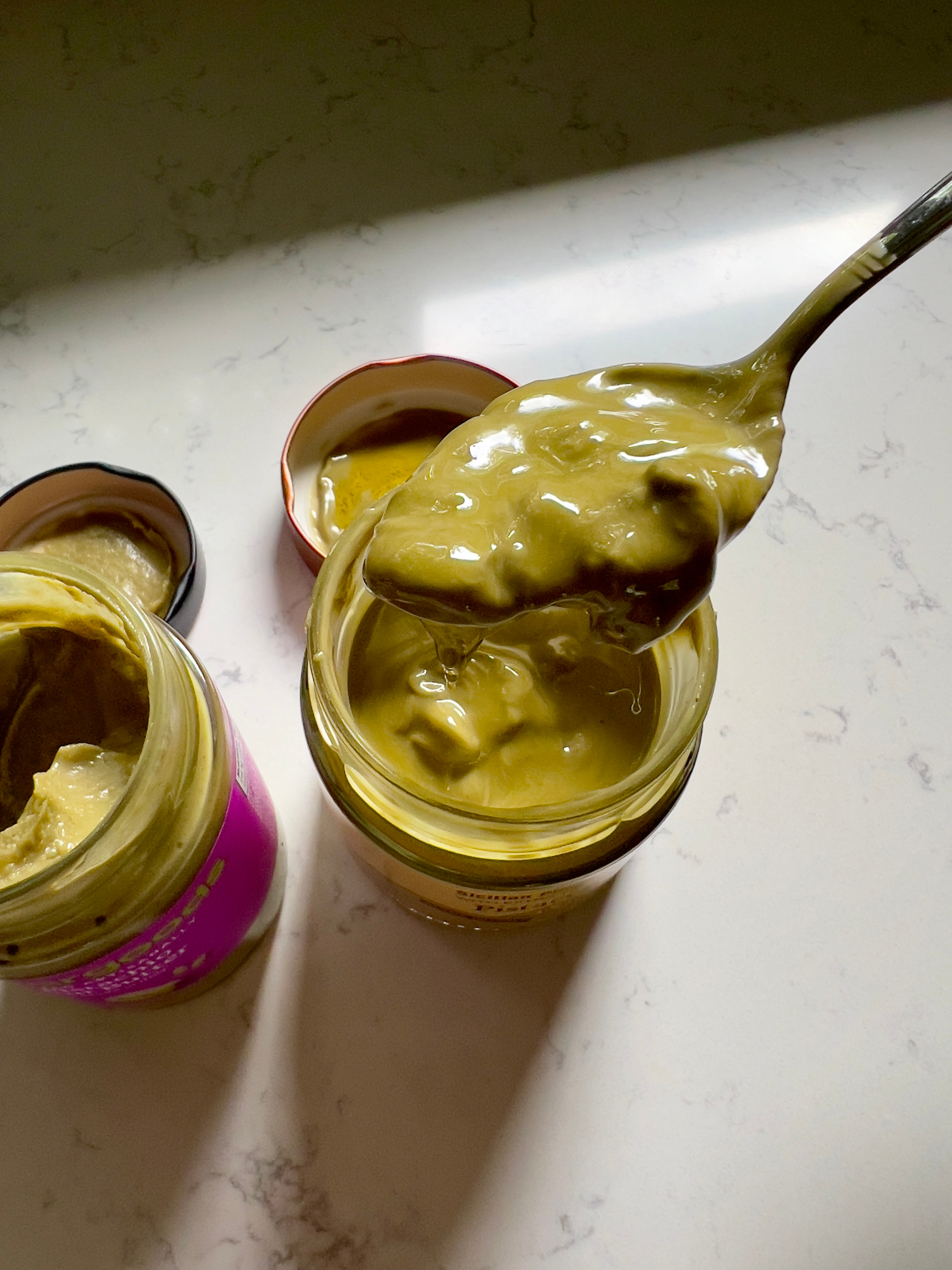 A spoon dipped in a jar of thick, creamy green sauce, resting on a countertop next to another opened jar