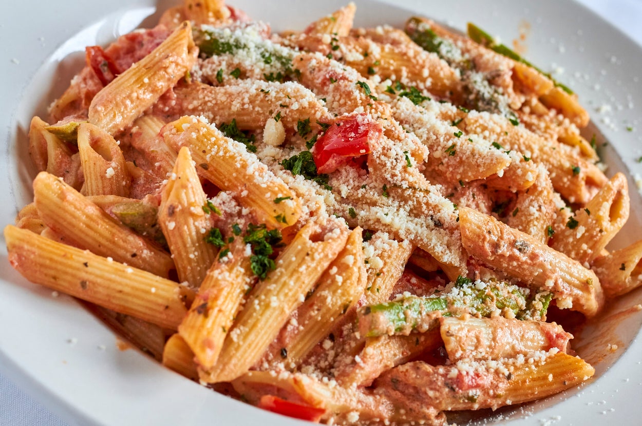 A bowl of penne pasta with creamy sauce, garnished with grated cheese and herbs