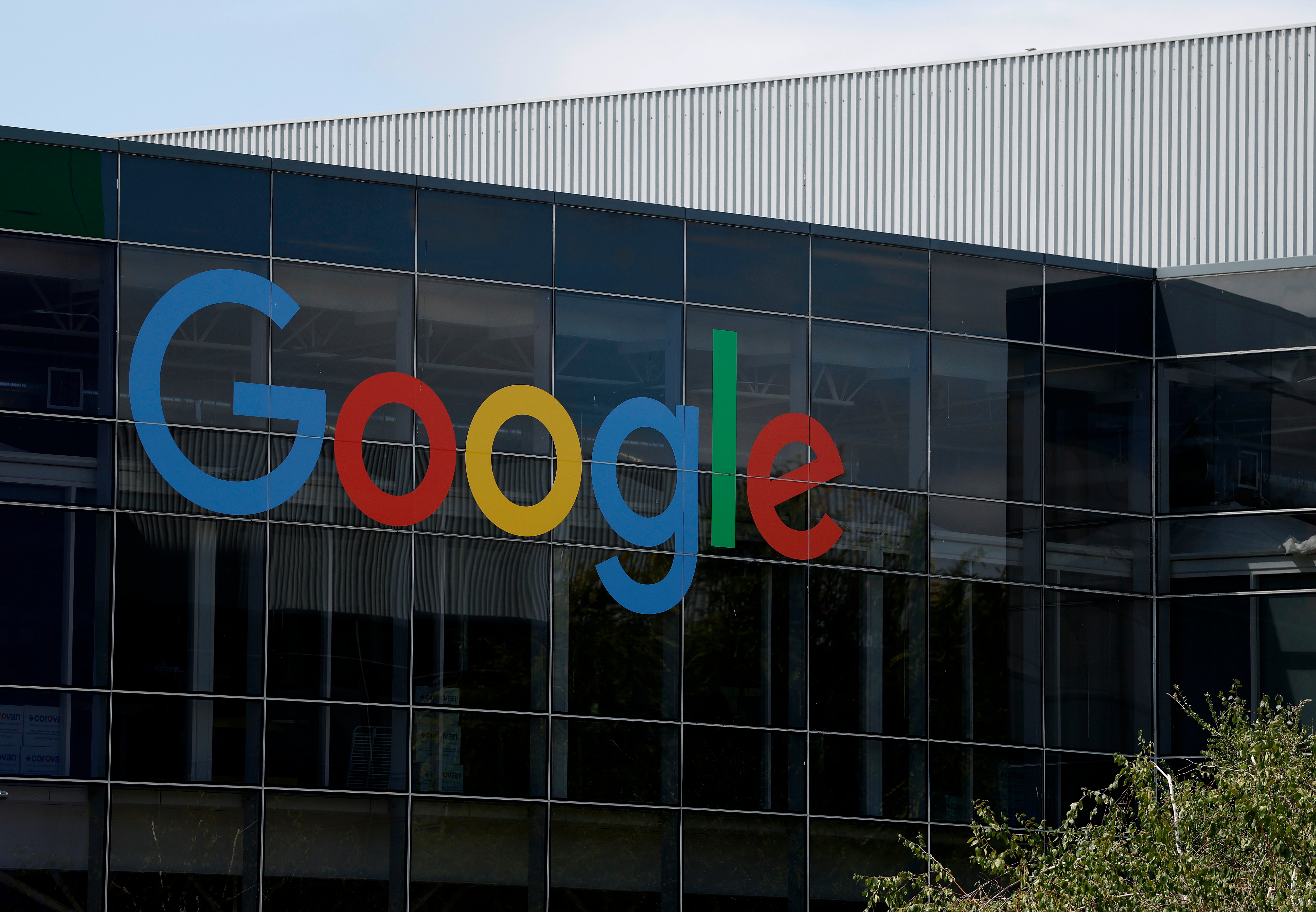 Google's logo on the exterior of a glass-paneled building, reflecting nearby surroundings