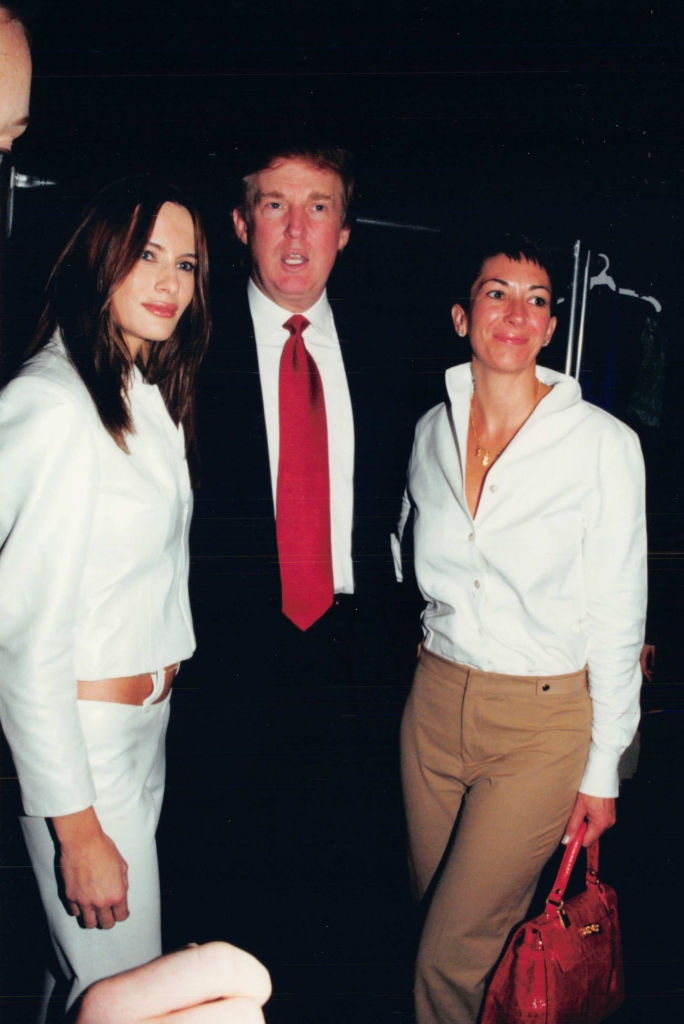 Three people in formal attire stand together, two in white tops and one in a suit with a red tie. They pose for a photo in an interior setting