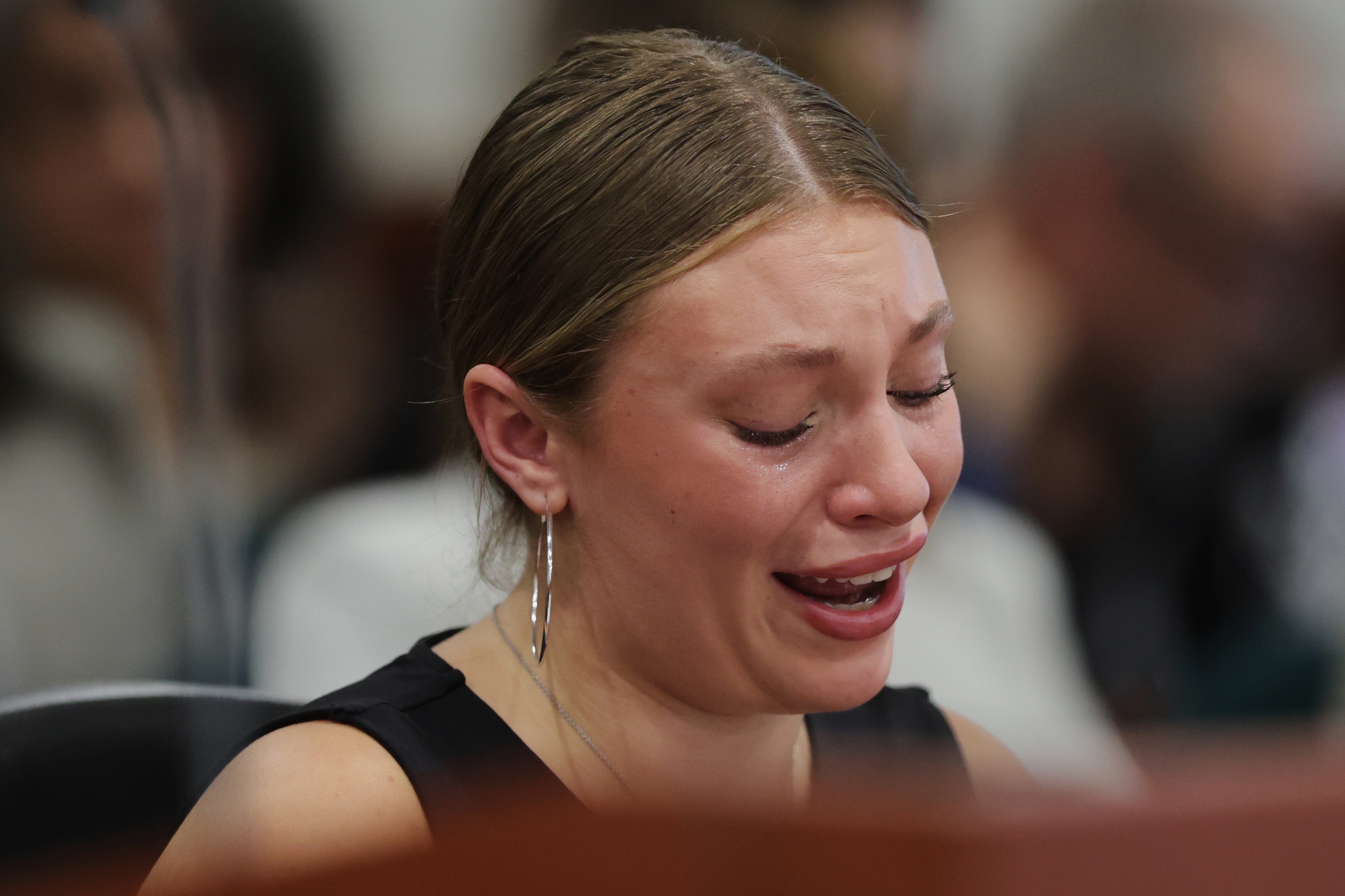 A person in emotional distress, crying, with hair pulled back and wearing hoop earrings, seated in a formal setting