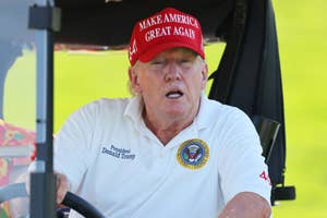 A person wearing a "Make America Great Again" hat and a white polo shirt with presidential insignia is sitting in a golf cart