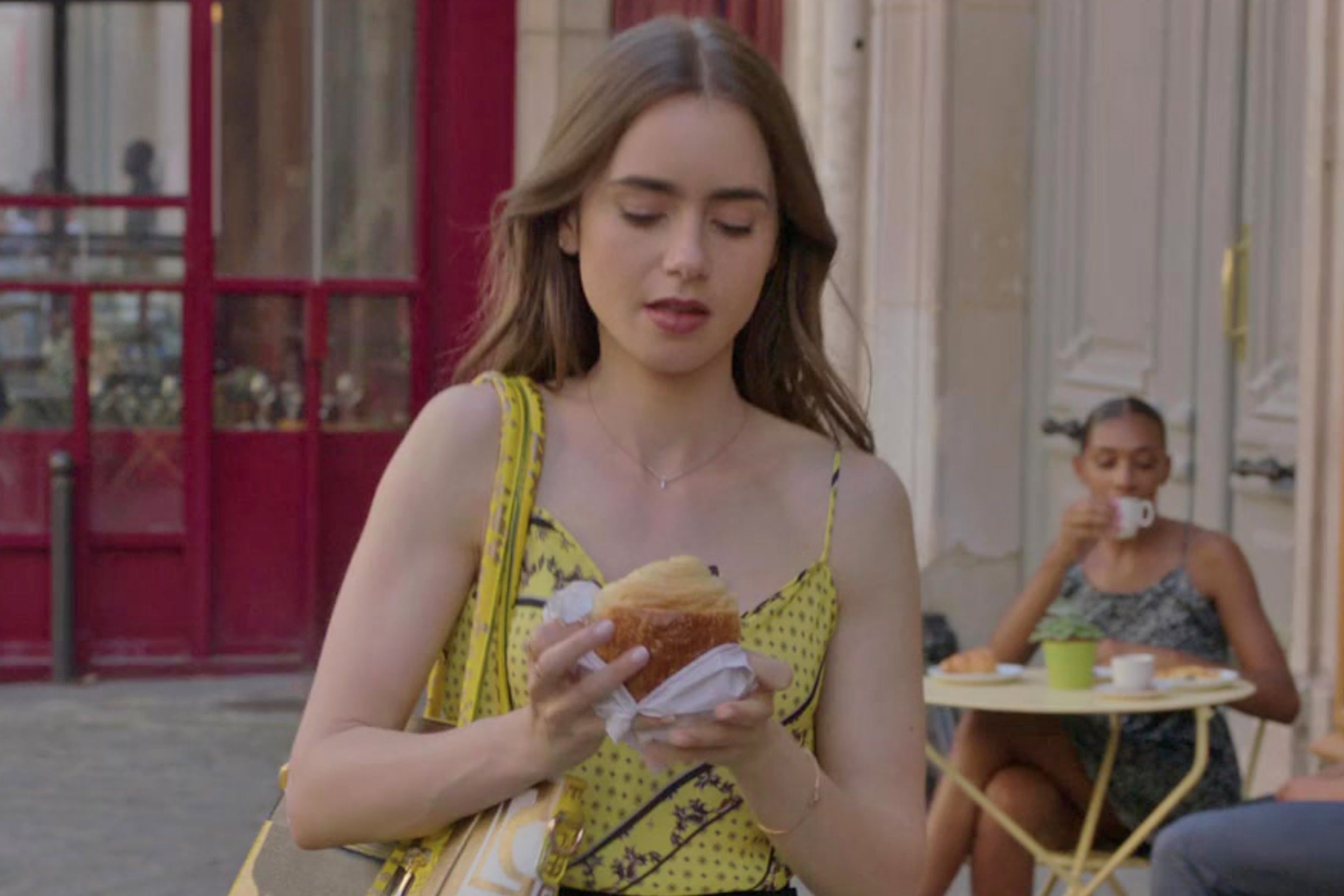 Emily from Emily in Paris walking around holding a croissant