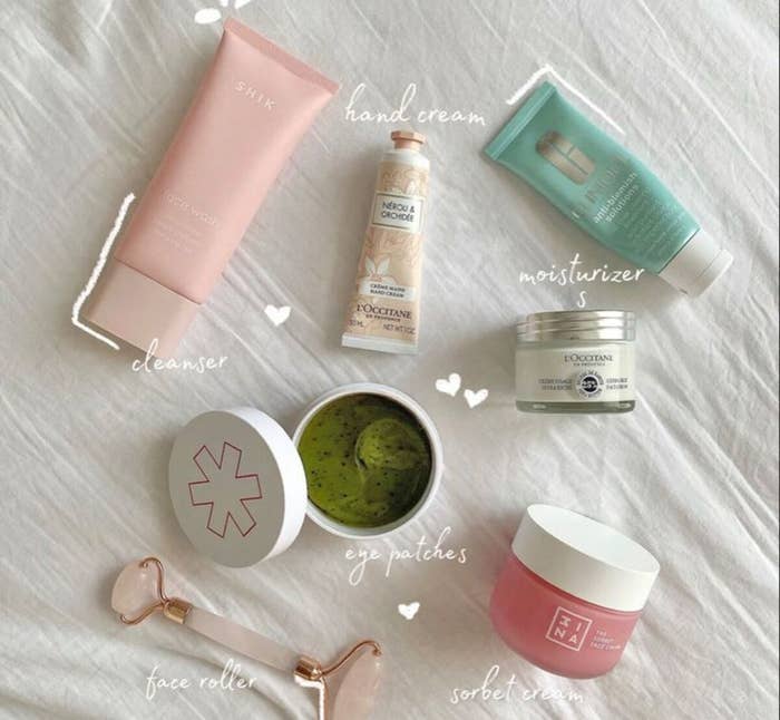 Set de cuidado de la piel sobre una superficie blanca: limpiador, crema de manos, humectante, parches de ojos, sorbete y rodillo facial