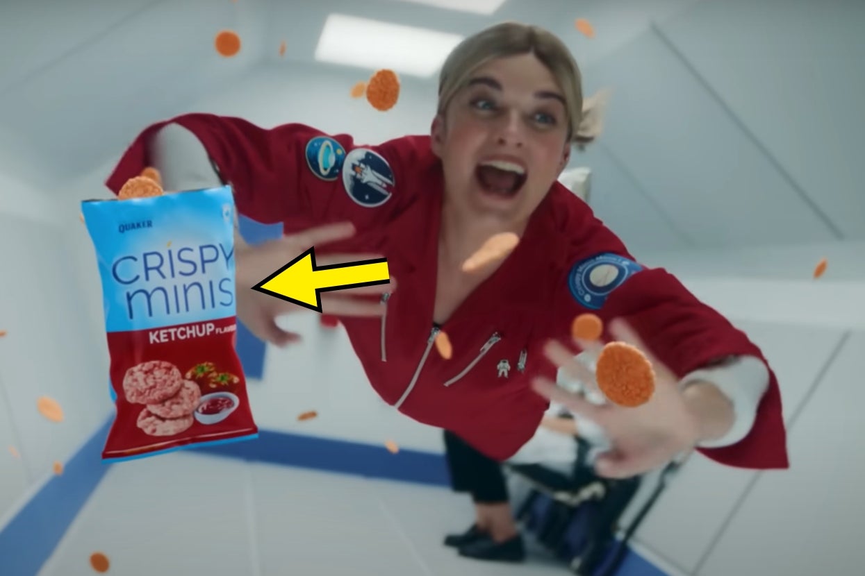 Annie Murphy floating in zero gravity reaches for a pack of ketchup-flavored crispy snacks