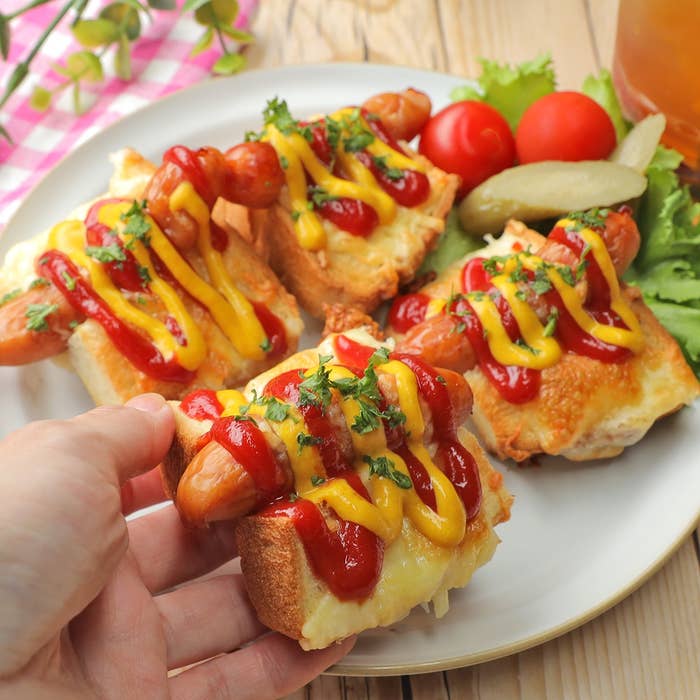 パンにケチャップとマスタードがかかった料理。トマトやピクルスが添えられている。