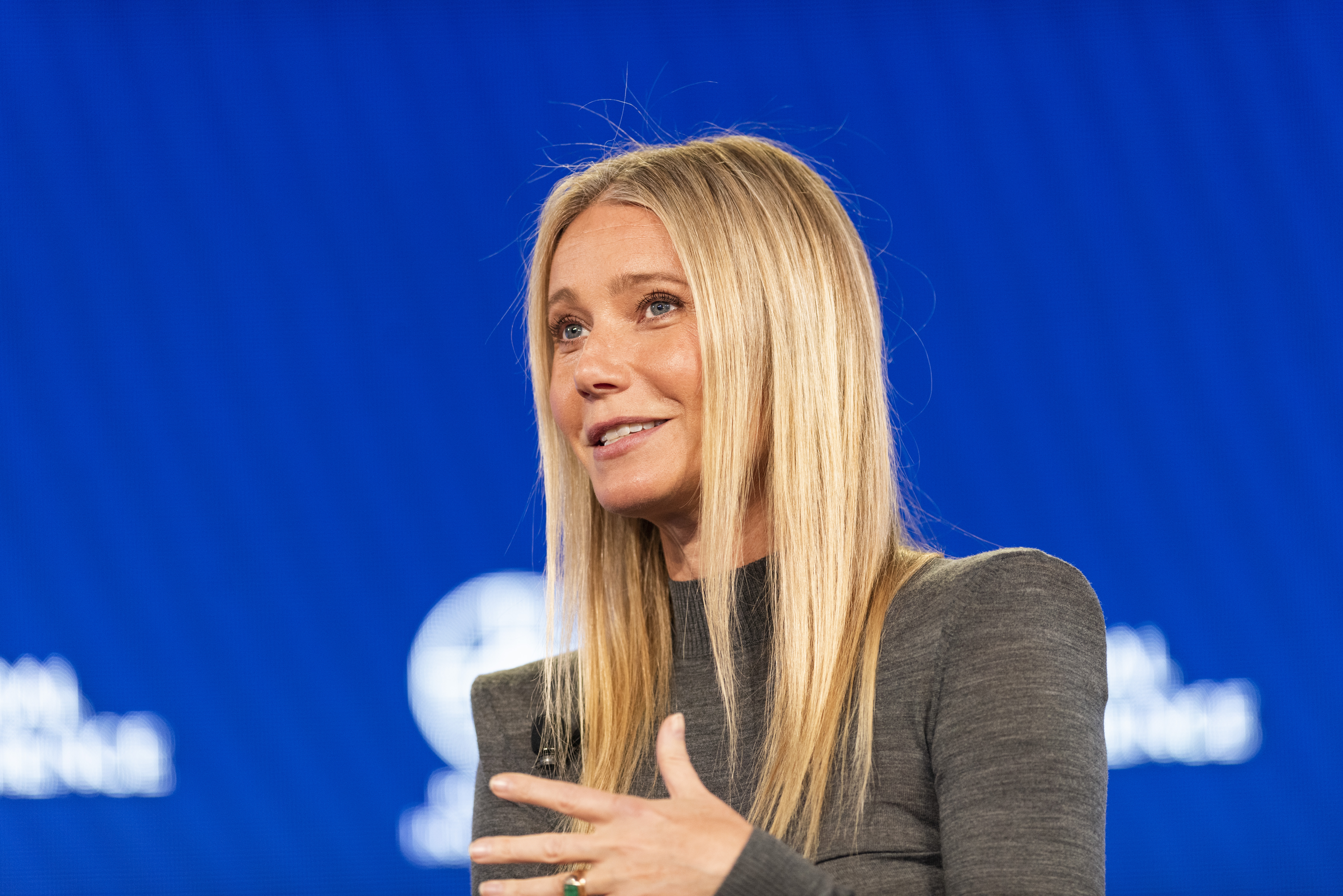 Gwyneth Paltrow speaking on stage, wearing a tailored dress, gesturing with one hand
