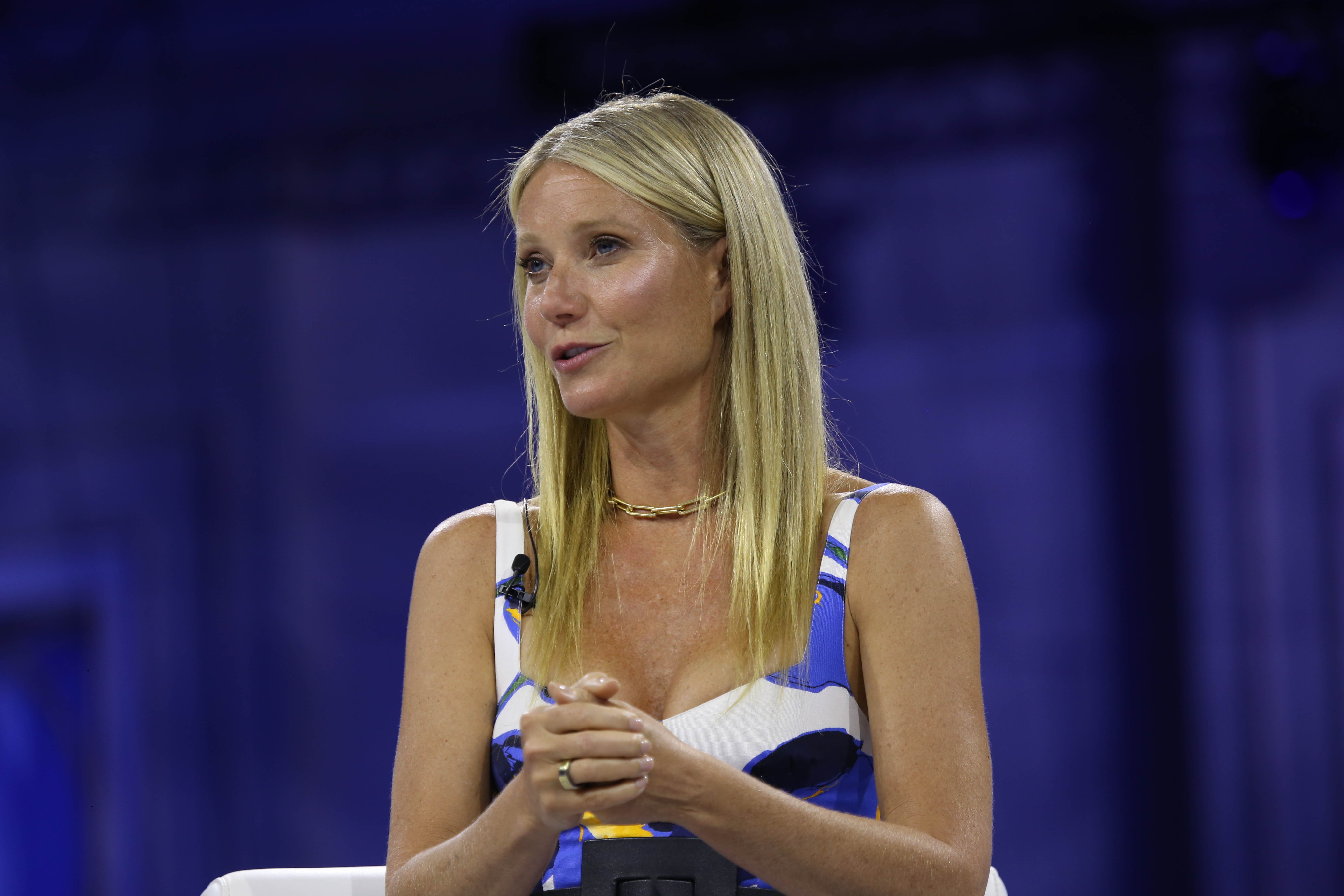 Gwyneth Paltrow in a fashionable dress speaks on stage with a focused expression