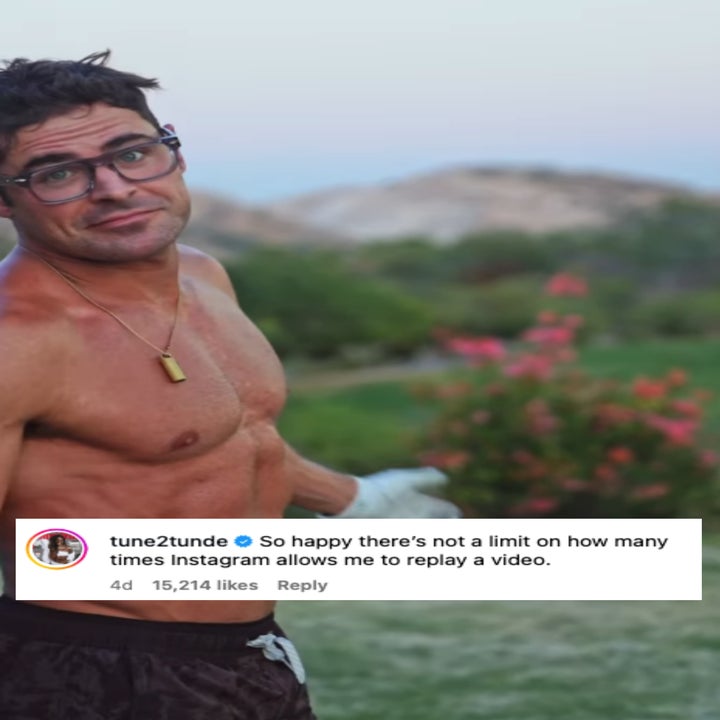 A man outdoors, shirtless, wearing glasses and a gold necklace, stands confidently with a glove on one hand, scenic hills in the background