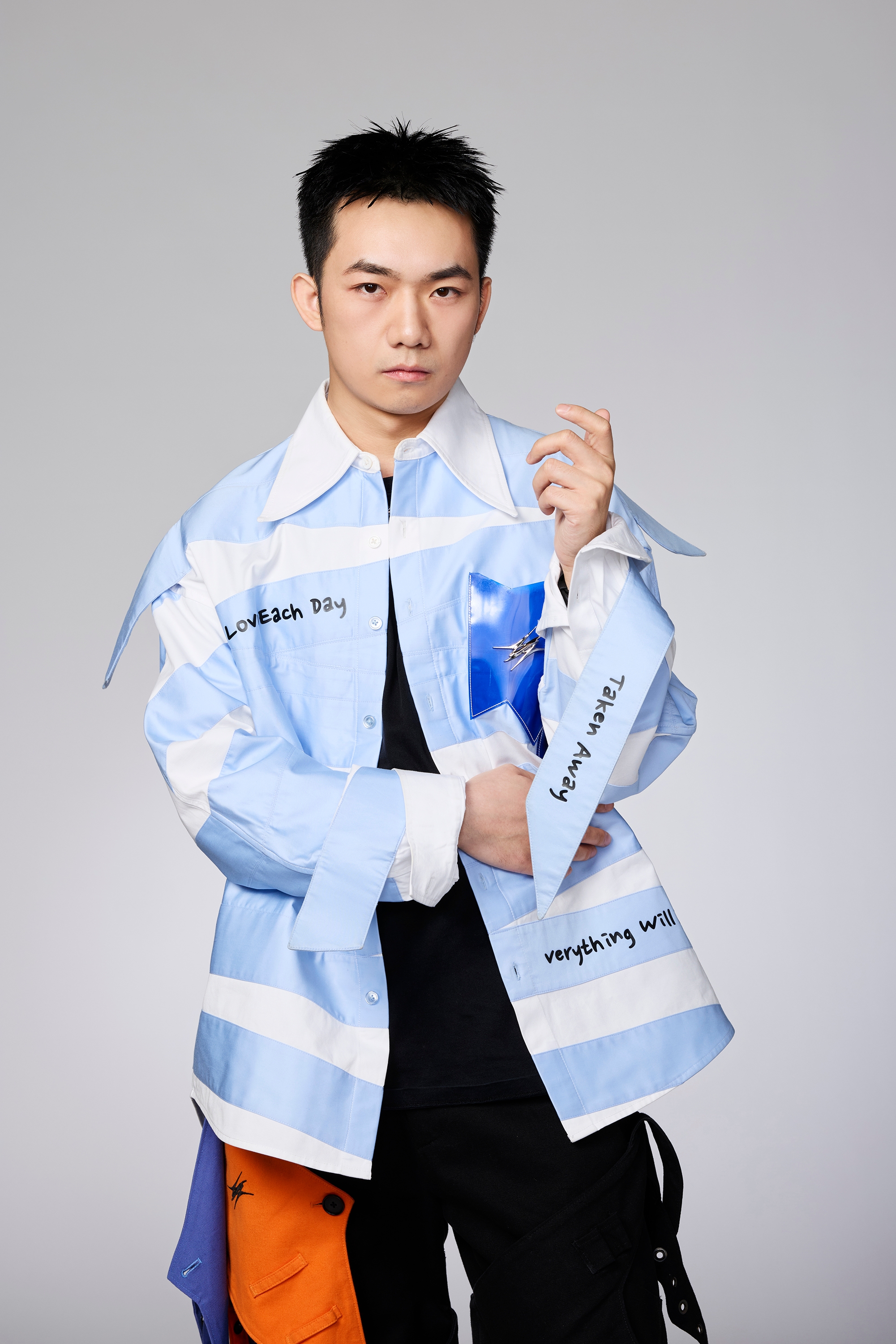 A person in a stylish, modern outfit featuring text and asymmetrical design poses confidently in front of a plain background