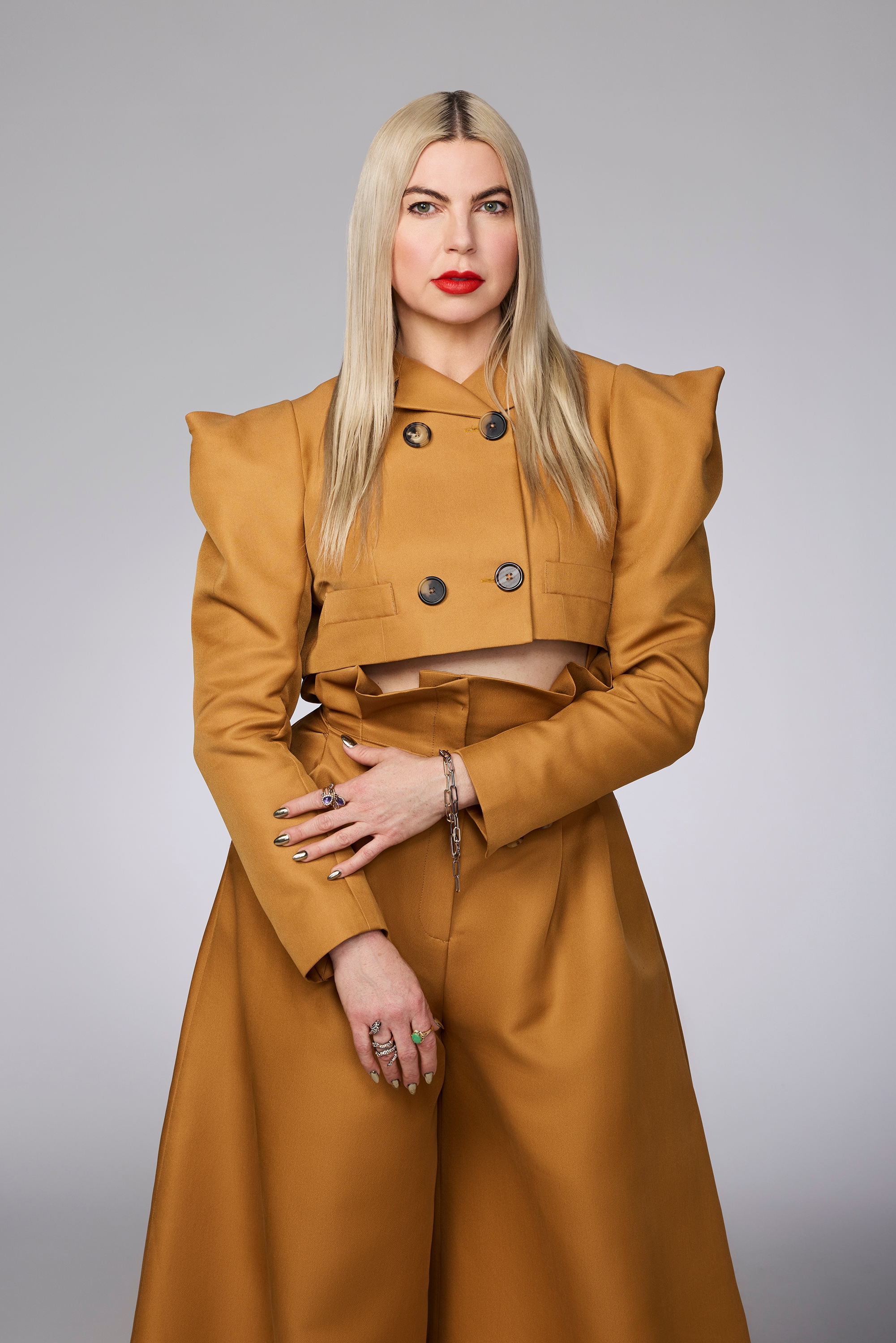 Person with long hair in structured, cropped double-breasted jacket and matching high-waisted skirt poses against a neutral background