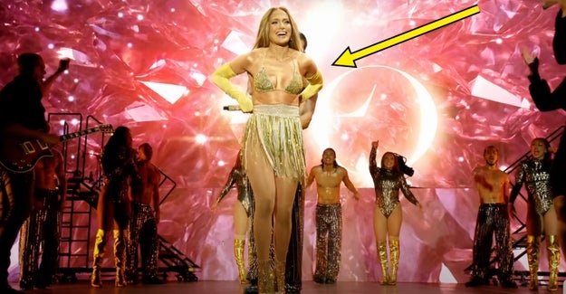 Performer on stage in a golden costume with dancers in glitter outfits in the background, set against a sparkling backdrop