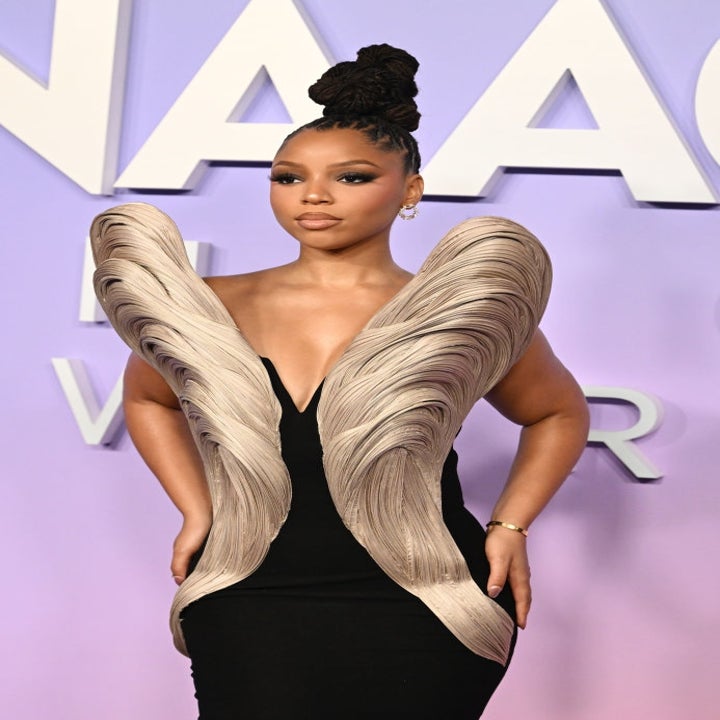 Person wearing a black dress with dramatic wave-like shoulder designs at a formal event. Hair styled in a high bun