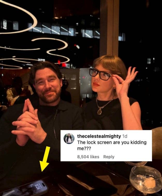Two people sit at a restaurant table, one showing a phone lock screen featuring someone else. The caption says, "The lock screen are you kidding me???"