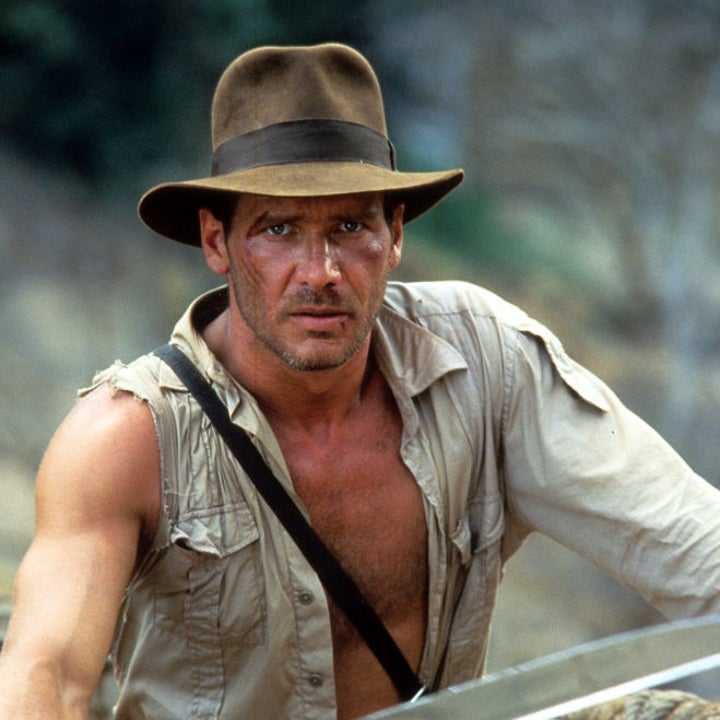 An adventurer wears a fedora, rugged shirt, and carries a machete while standing on a rope bridge, exuding a classic explorer vibe