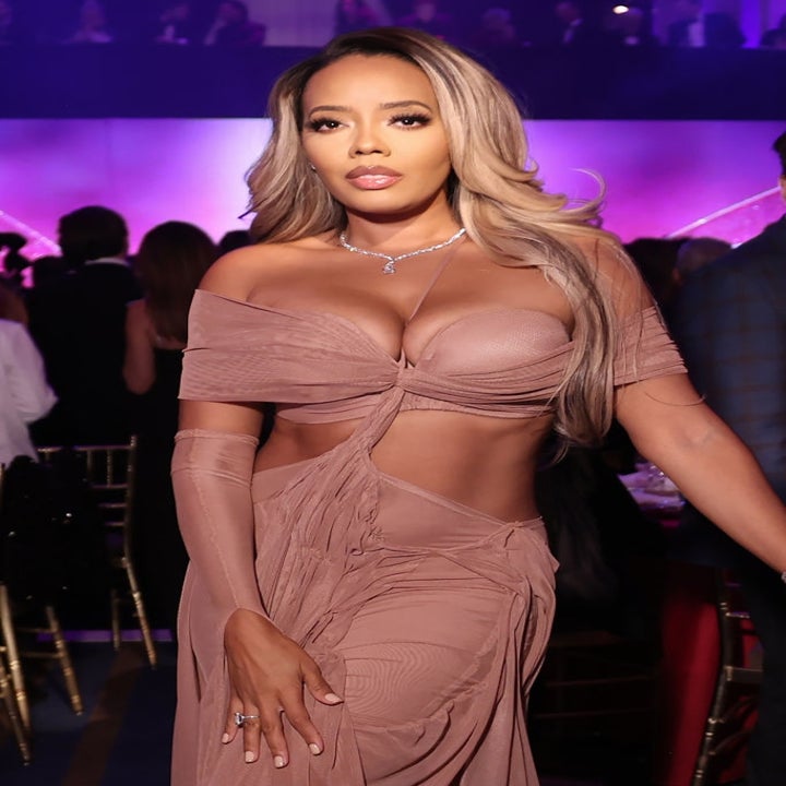 Person on the red carpet in an elegant, draped outfit with off-shoulder sleeves, wearing subtle jewelry and styled hair