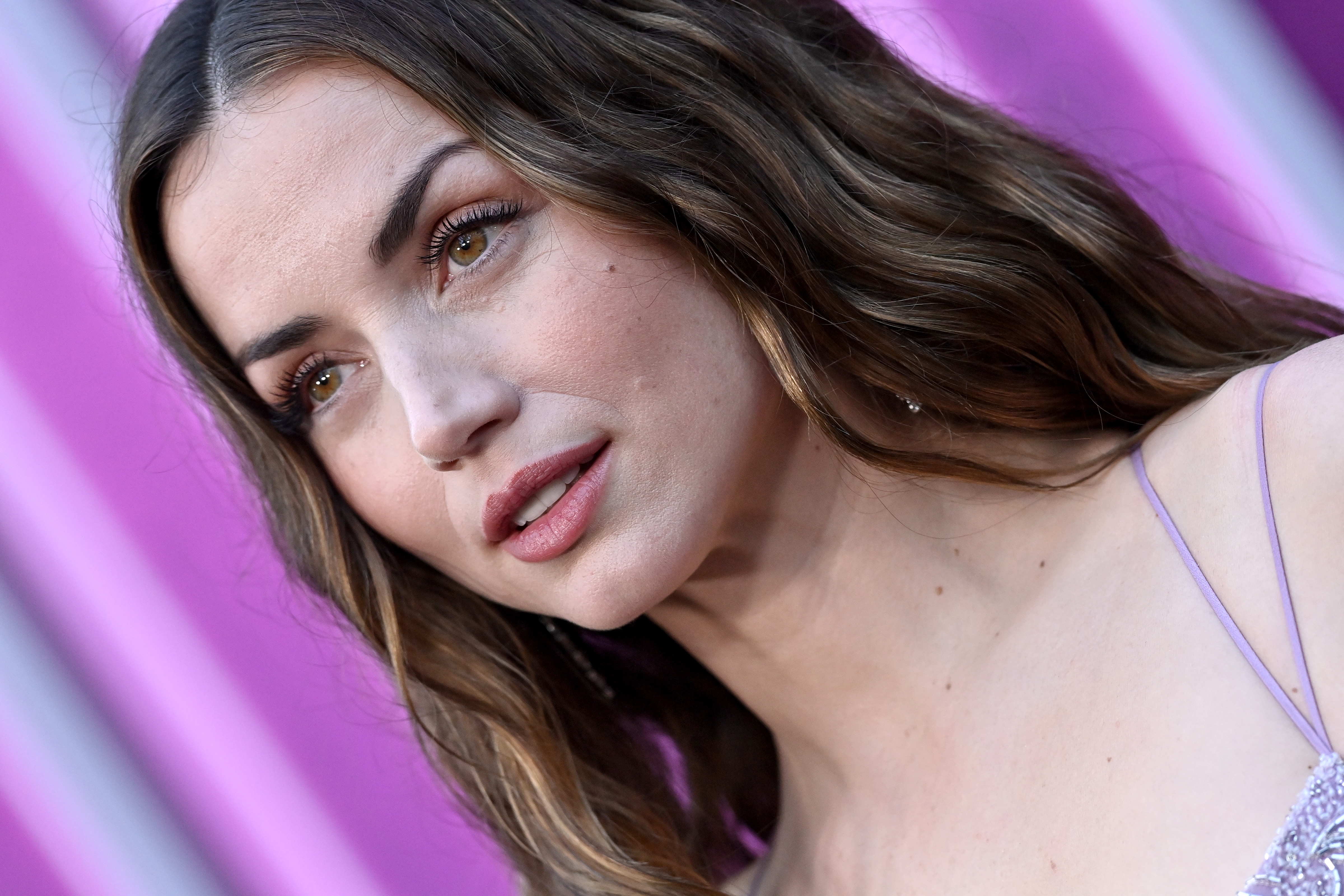 Ana De Armas with long wavy hair and spaghetti strap top poses in front of a vibrant background