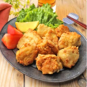 皿に盛られた唐揚げとレタス、トマト、レモンのスライス。食卓に箸とナプキンがある。