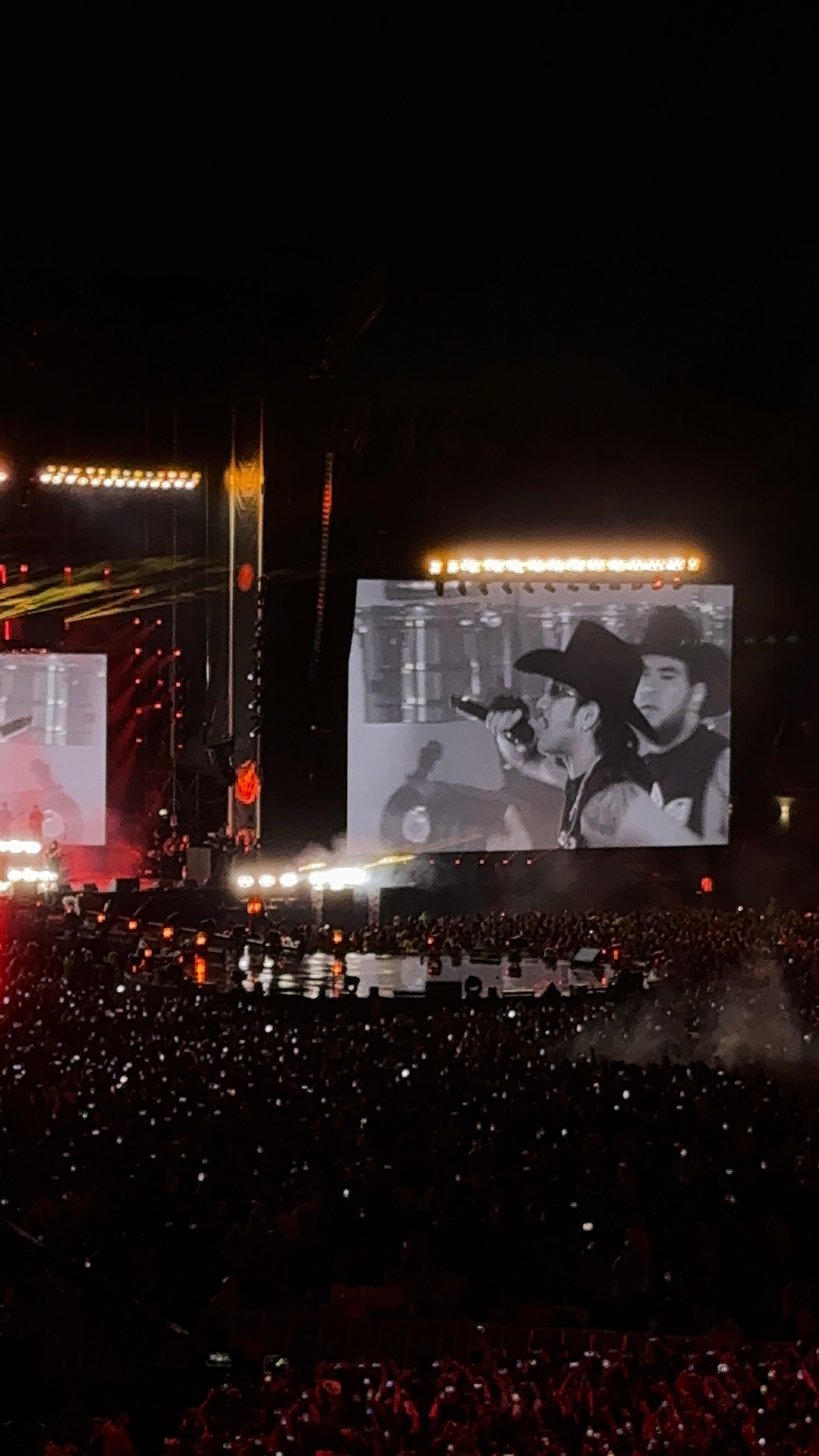 Concierto con cantantes en pantalla grande. Público mira el espectáculo. Ambiente energético en un evento de música en vivo