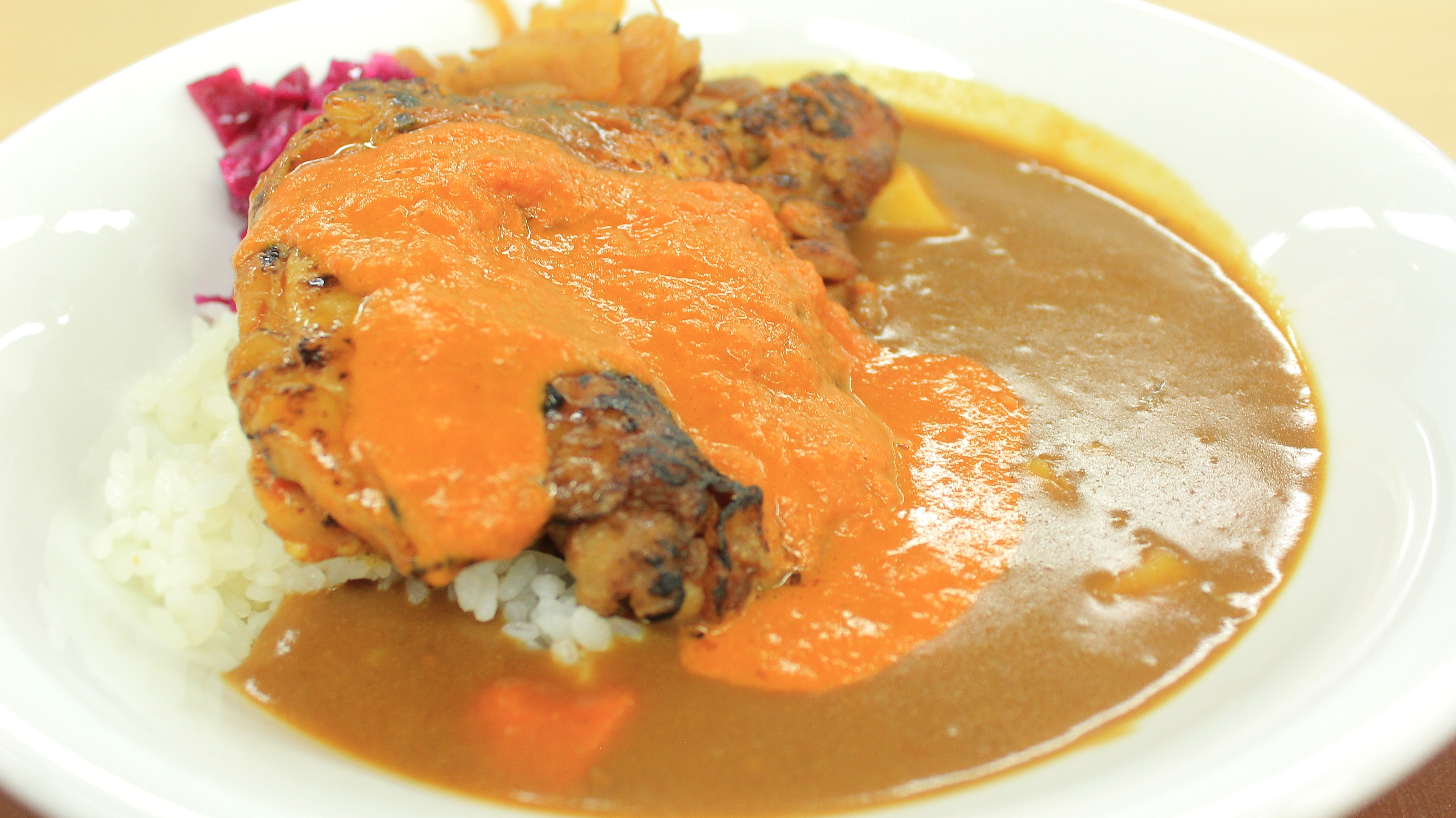 カレーライスにグリルチキンとオレンジソースがのった料理が白い皿に盛られています。